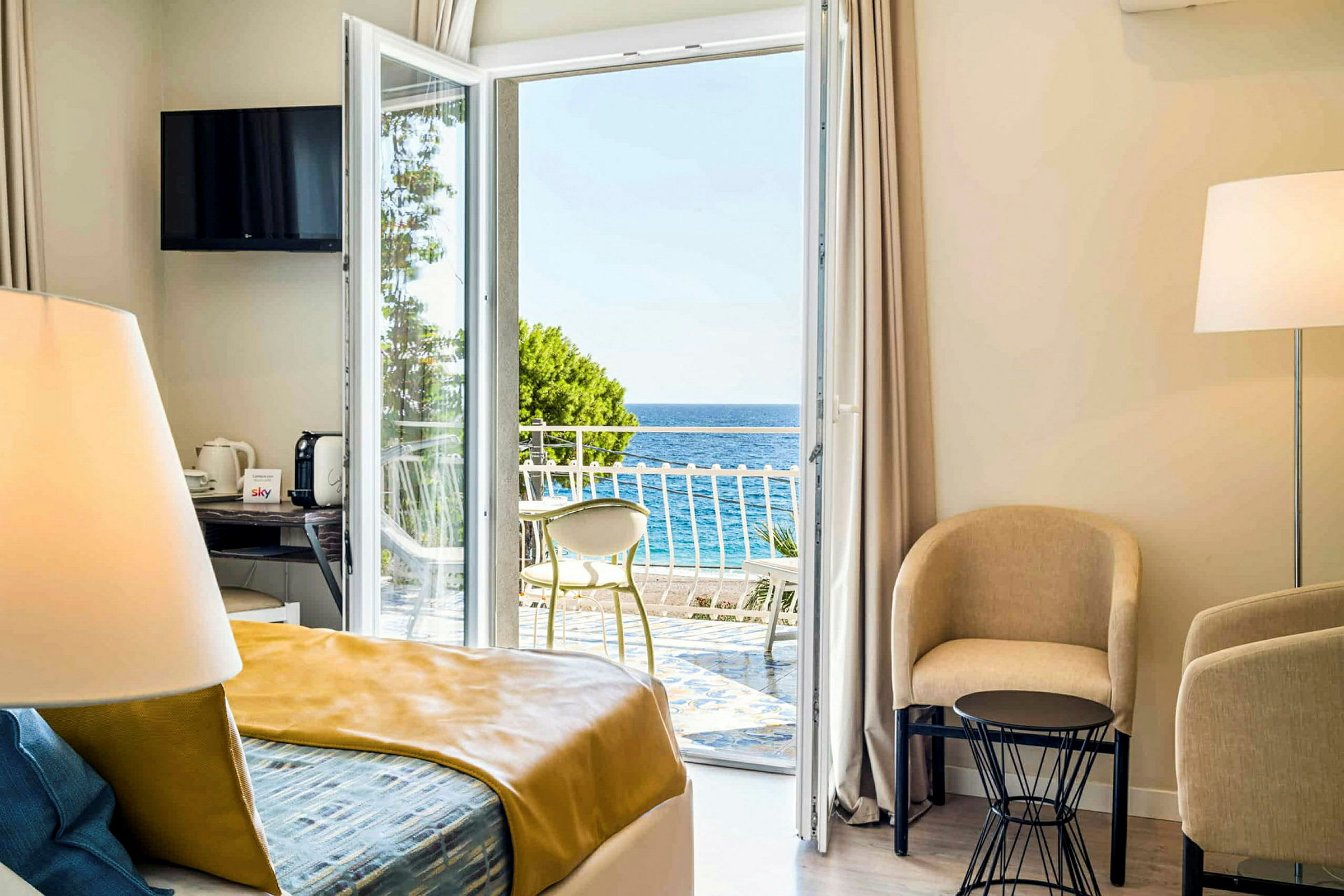 Et lyst hotelværelse med udsigt over havet gennem en åben altandør. (AI-genereret tekst)