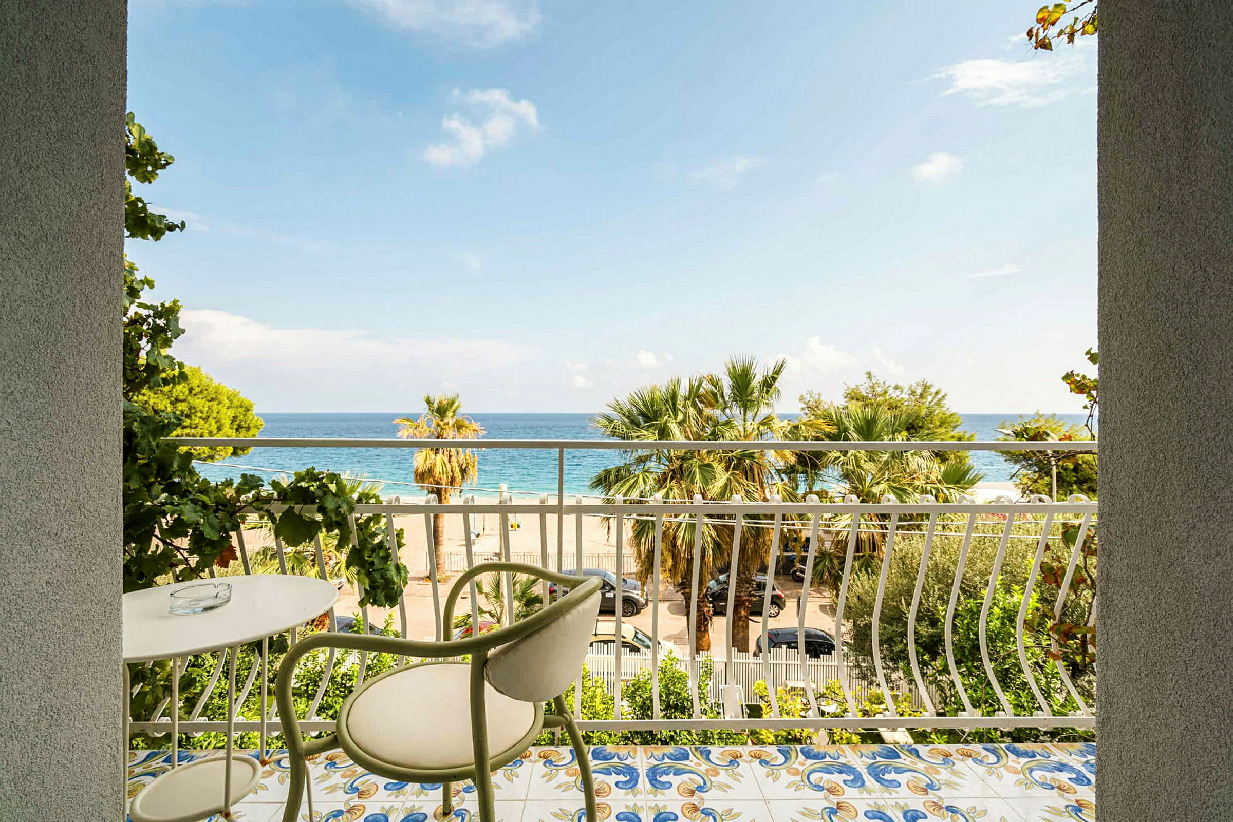En balkon med udsigt over stranden og havet. Balkonen har et bord og en stol. (AI-genereret tekst)