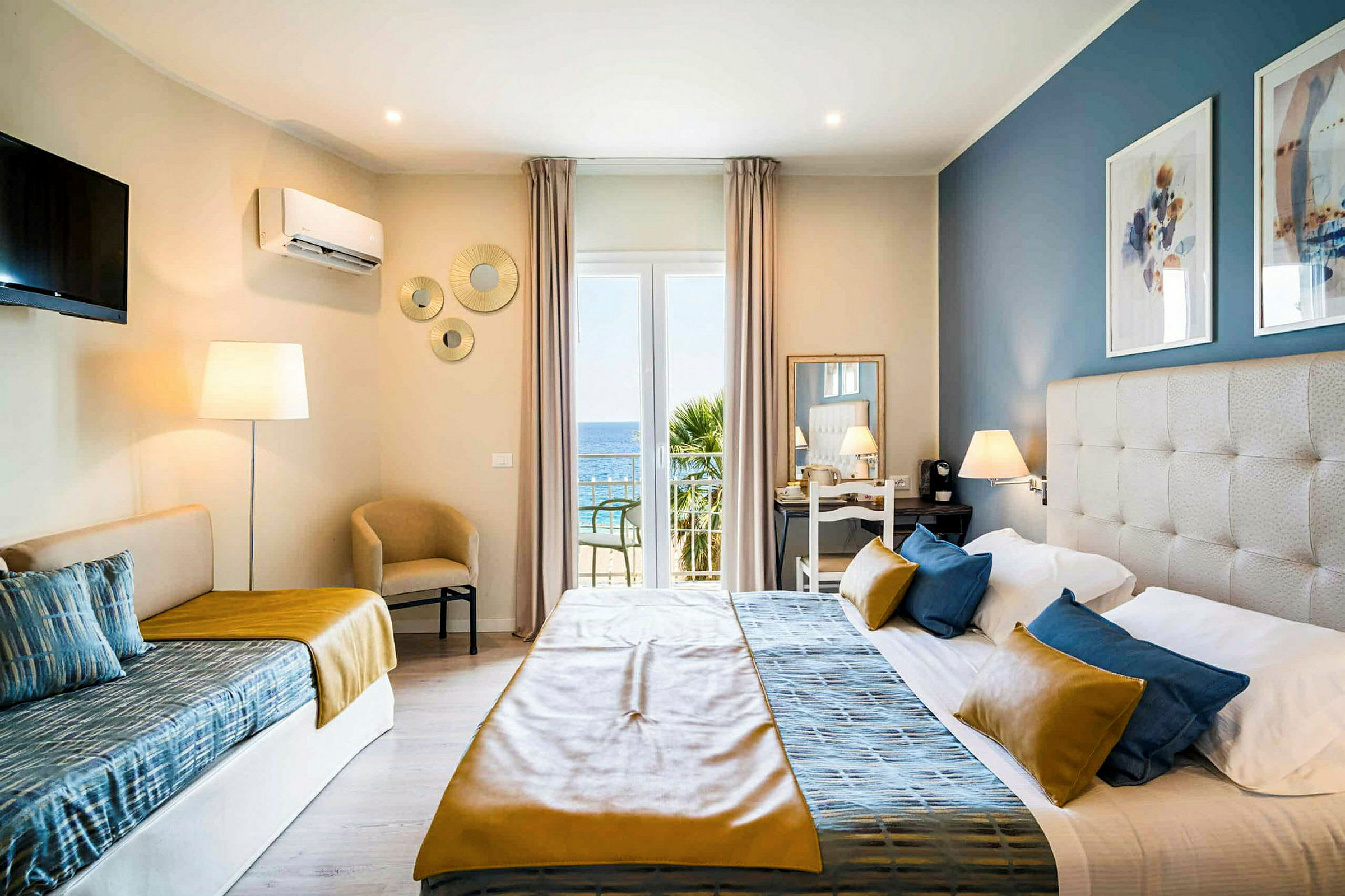 Et hotelværelse med en seng, en sofa og udsigt til havet gennem en glasdør. (AI-genereret tekst)