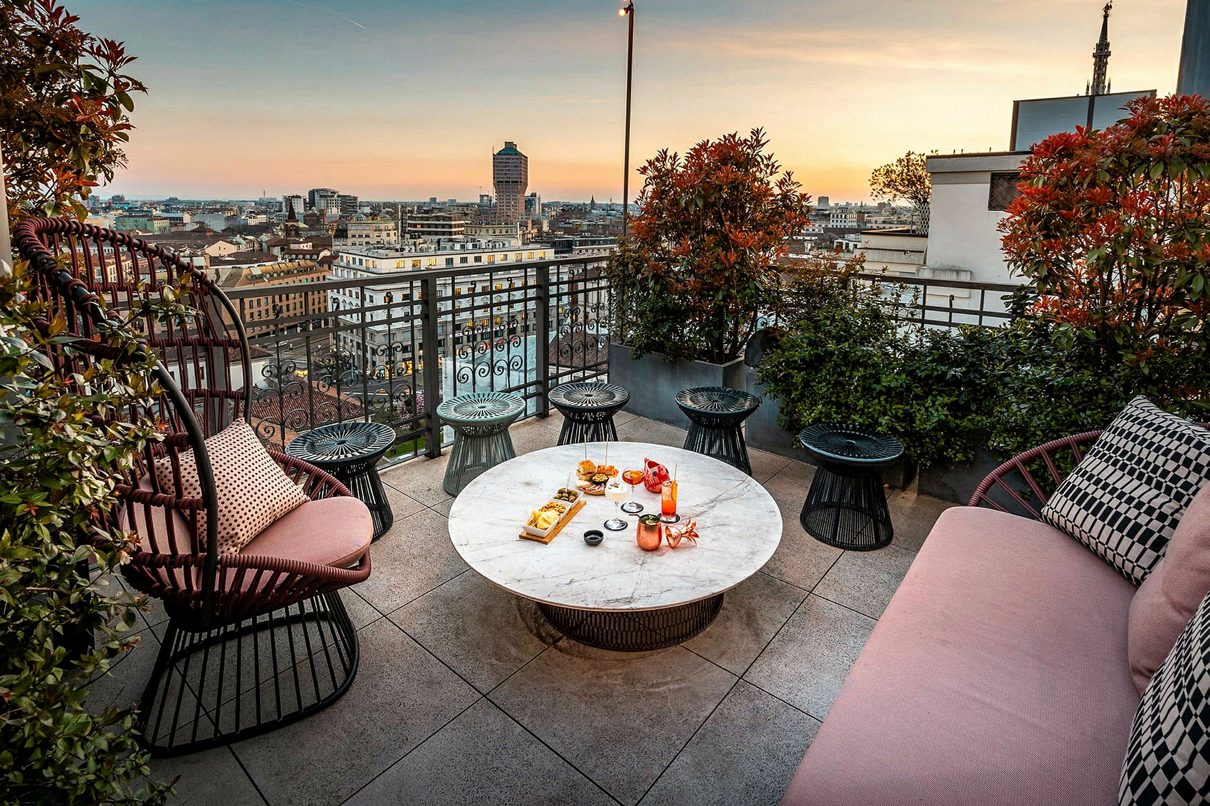 Terrasse med udsigt over byen ved solnedgang, møbler og bord med mad og drikke. (AI-genereret tekst)