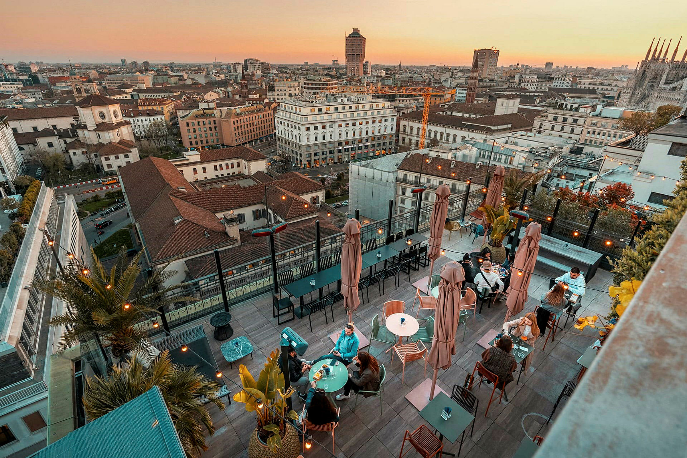 En tagterrasse med borde og siddepladser, omgivet af en panoramaudsigt over en by ved solnedgang. (AI-genereret tekst)