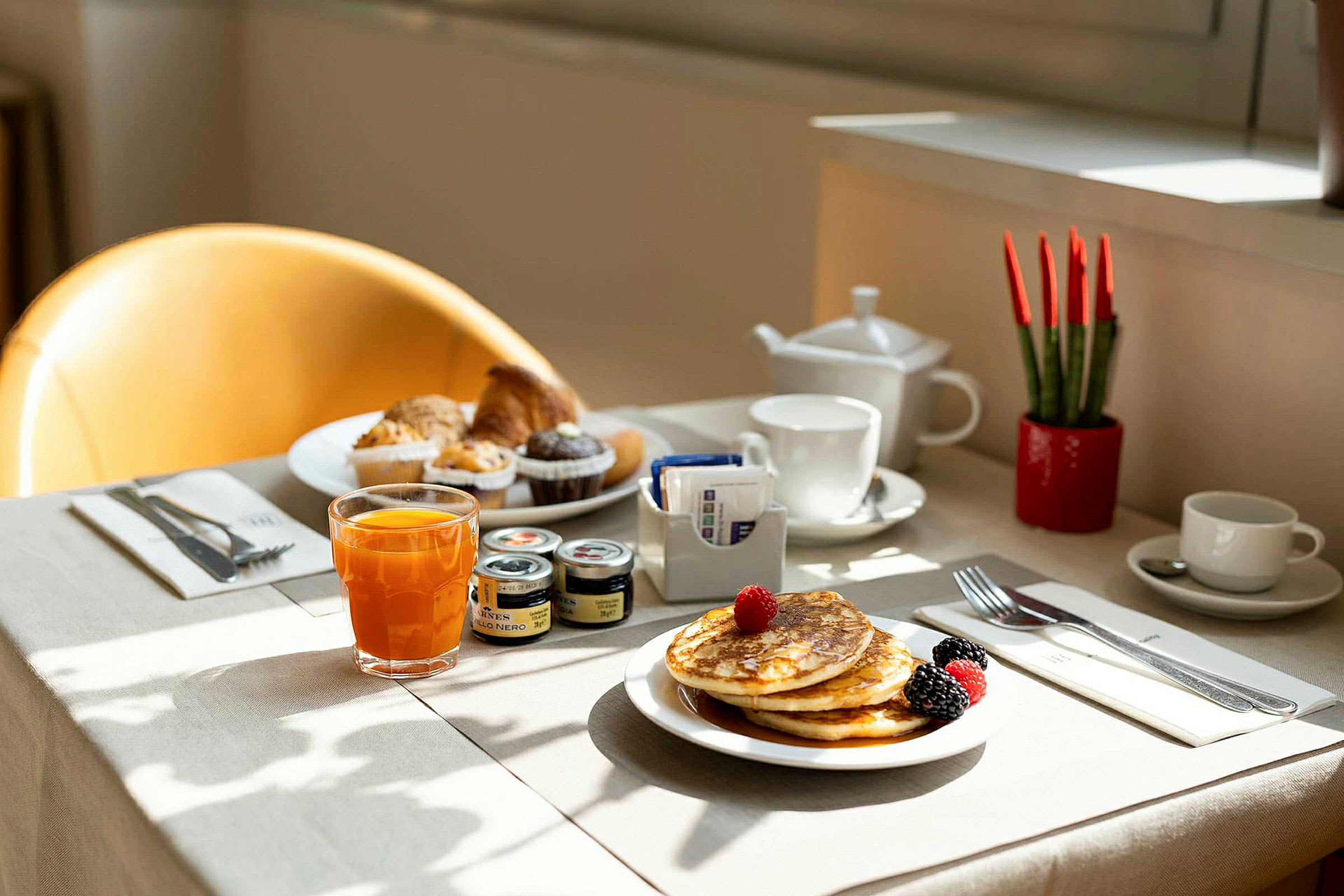 En dækket morgenmad med pandekager, frugt, juice og muffins på et bord. (AI-genereret tekst)