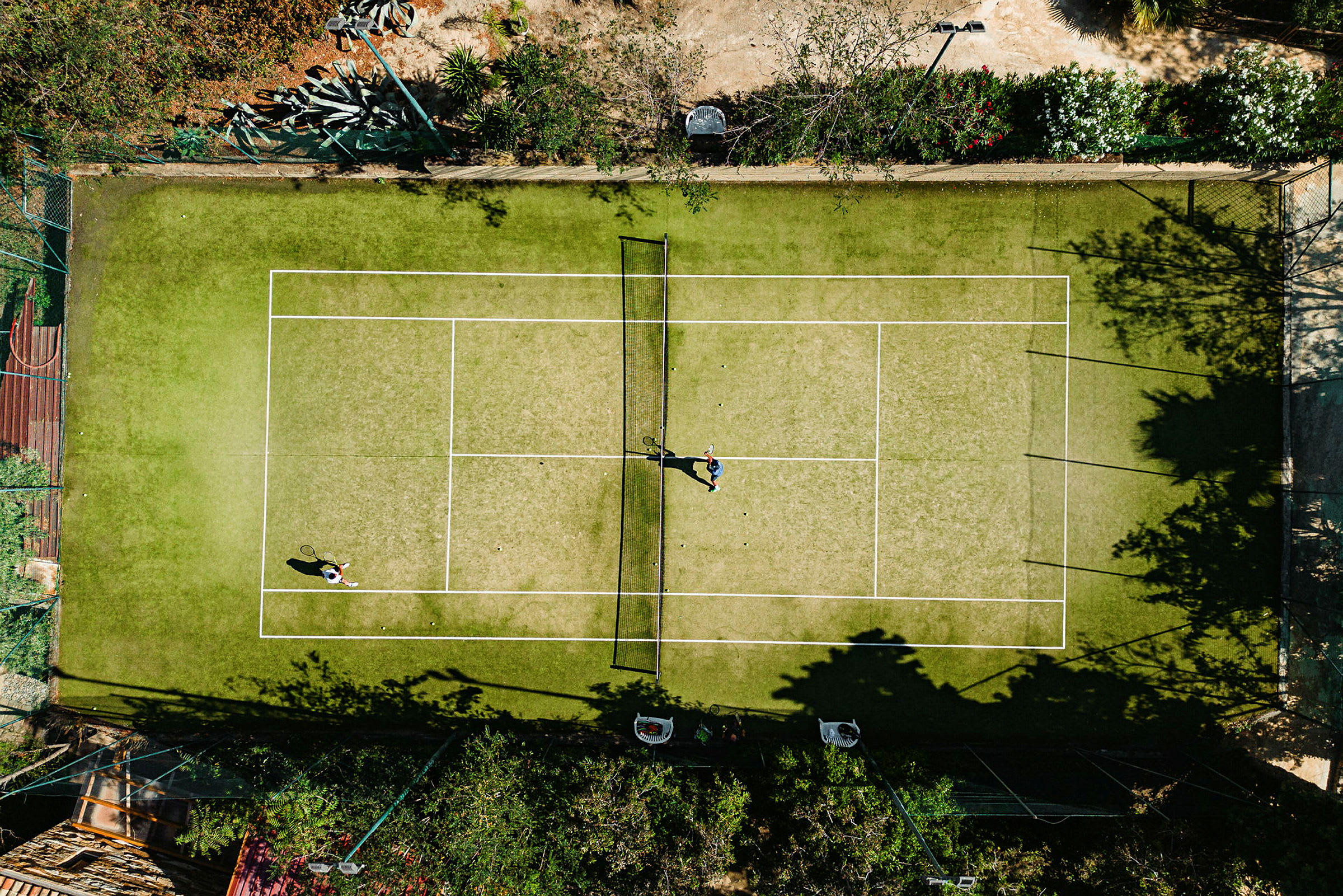 Luftfoto af to personer, der spiller tennis på en grusbane omgivet af vegetation. (AI-genereret tekst)