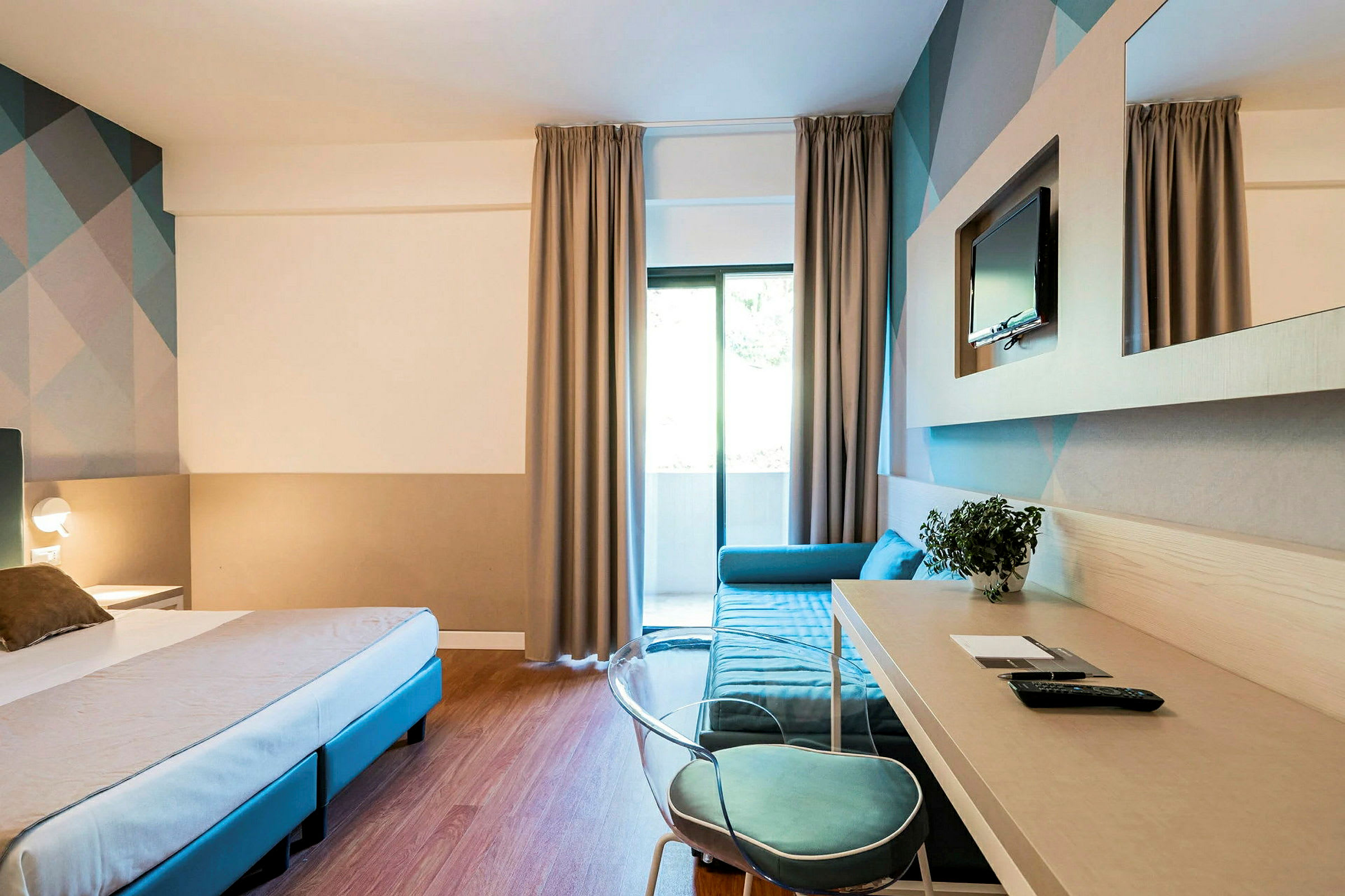 Hotelværelse med seng, skrivebord og sofa samt tv på væggen. (AI-genereret tekst)