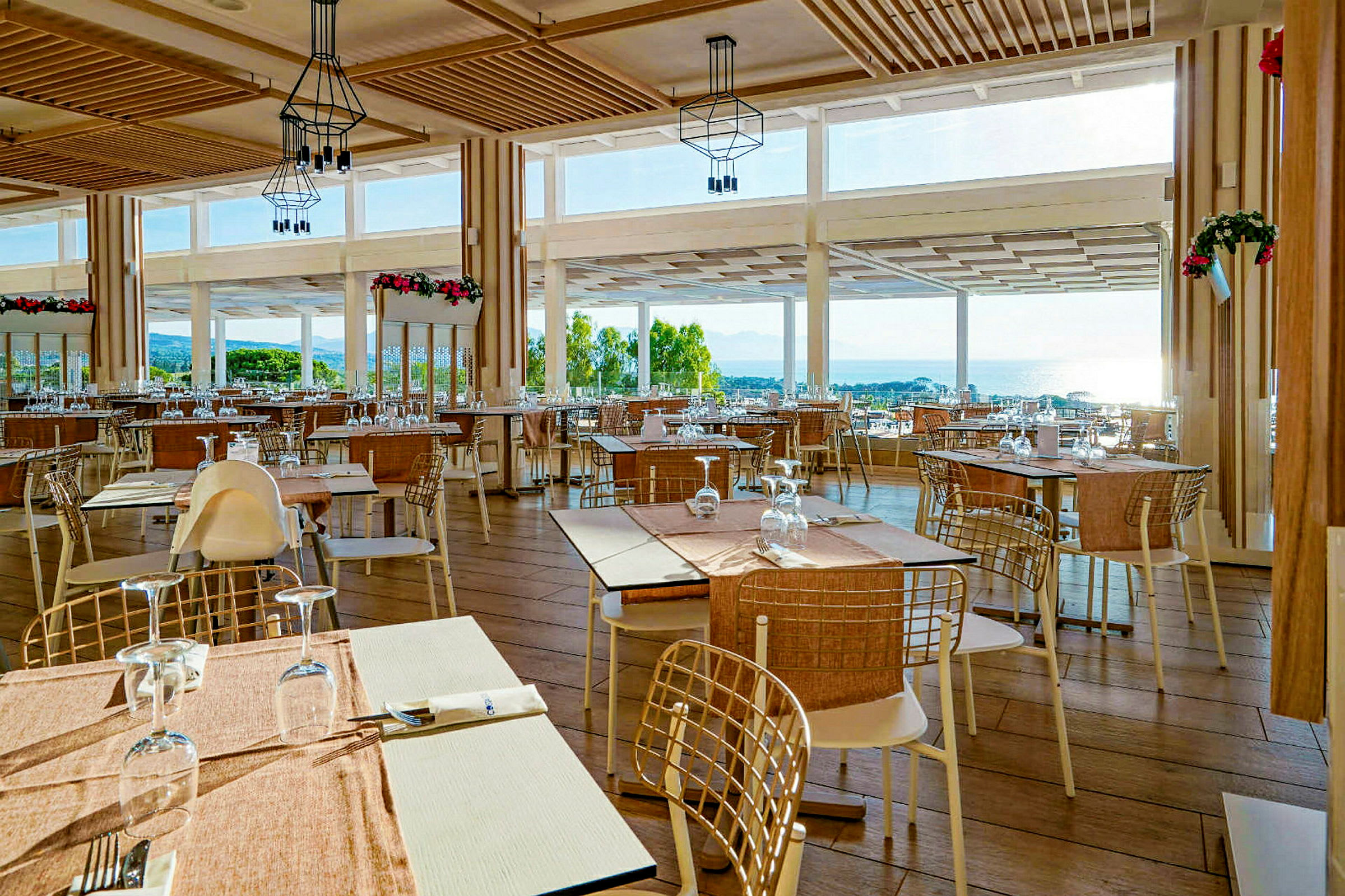 En restaurant med borde og stole, store vinduer med udsigt over landskabet og havet. (AI-genereret tekst)