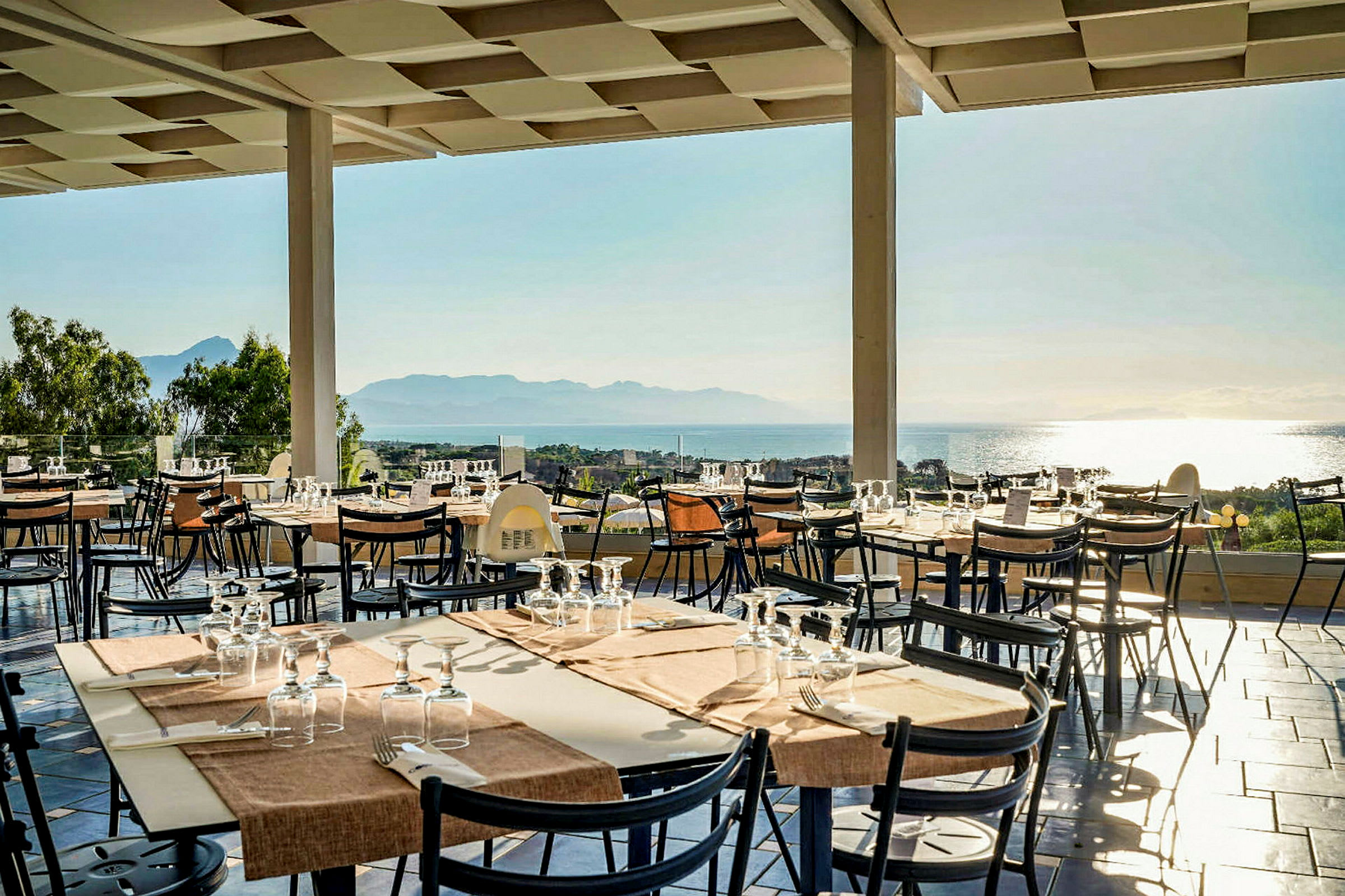 Terrasse med dækkede borde og udsigt over havet. (AI-genereret tekst)