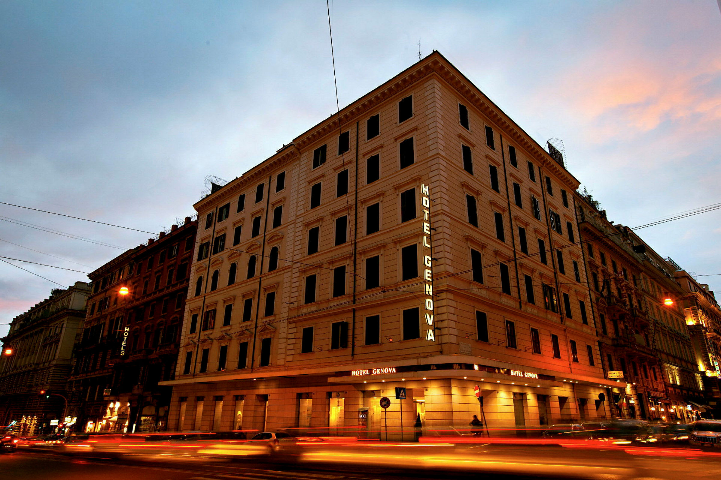 En fleretagers bygning med teksten Hotel Genova oplyst på facaden. (AI-genereret tekst)