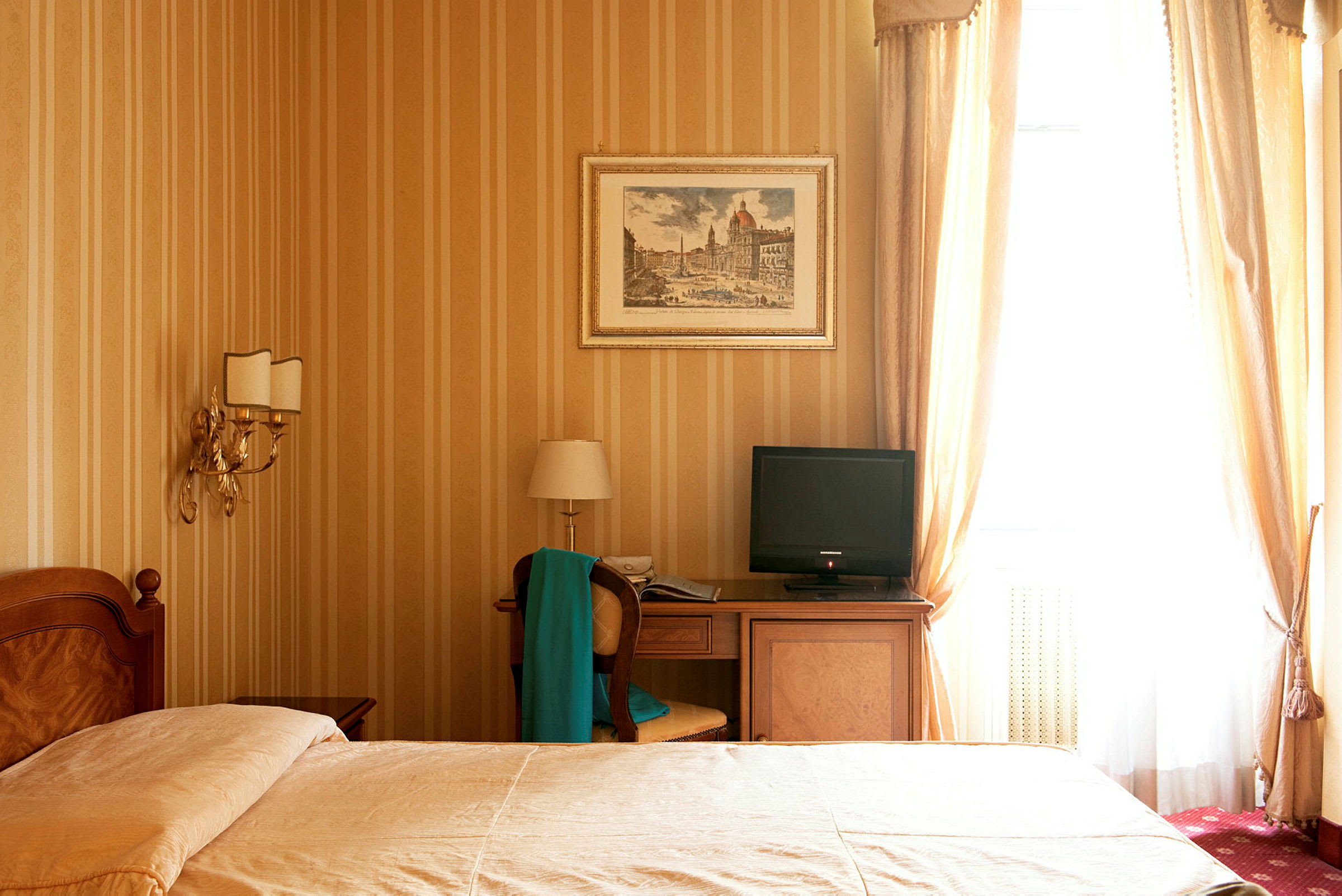 Et hotelværelse med en seng, natbord, skrivebord med en stol og et TV samt guldtonede vægge og gardiner. (AI-genereret tekst)