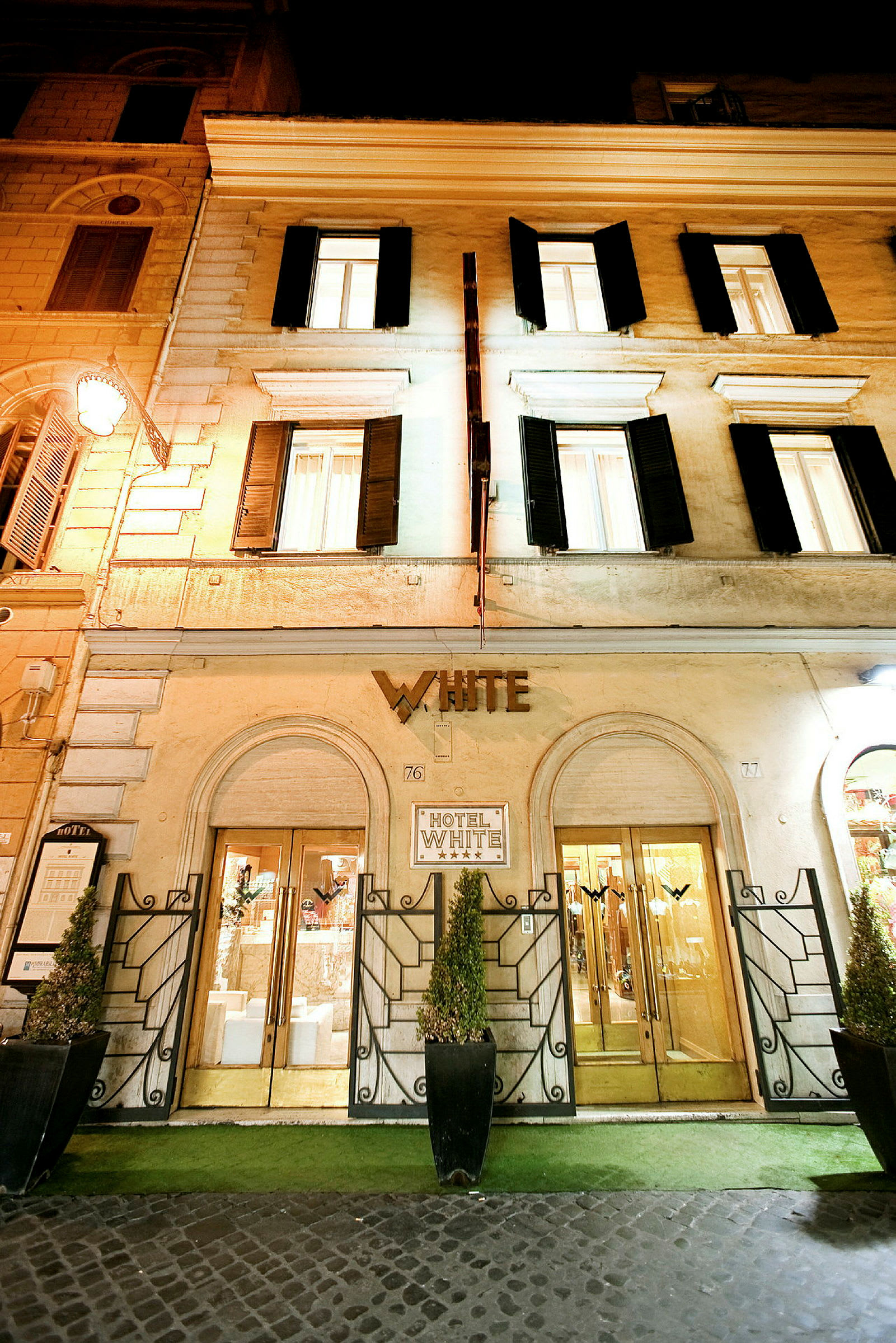 Hotellets facade med navnet 'White' over indgangen, markante døråbninger og pyntelige planter. (AI-genereret tekst)