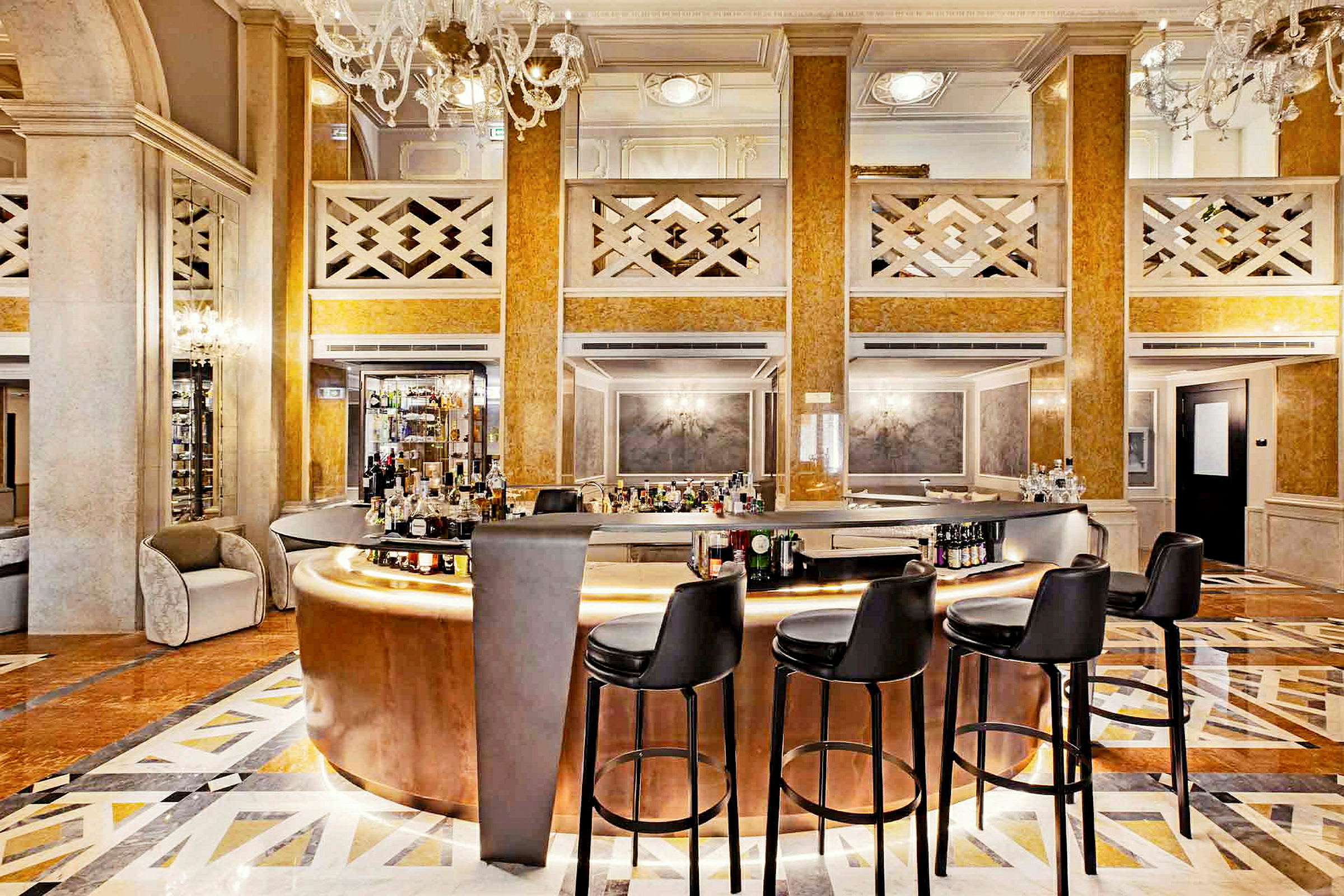 En elegant hotelbar med polerede guldfarvede materialer og en velholdt gulvflade, omringet af sorte barstole og elegante lysekroner. (AI-genereret tekst)