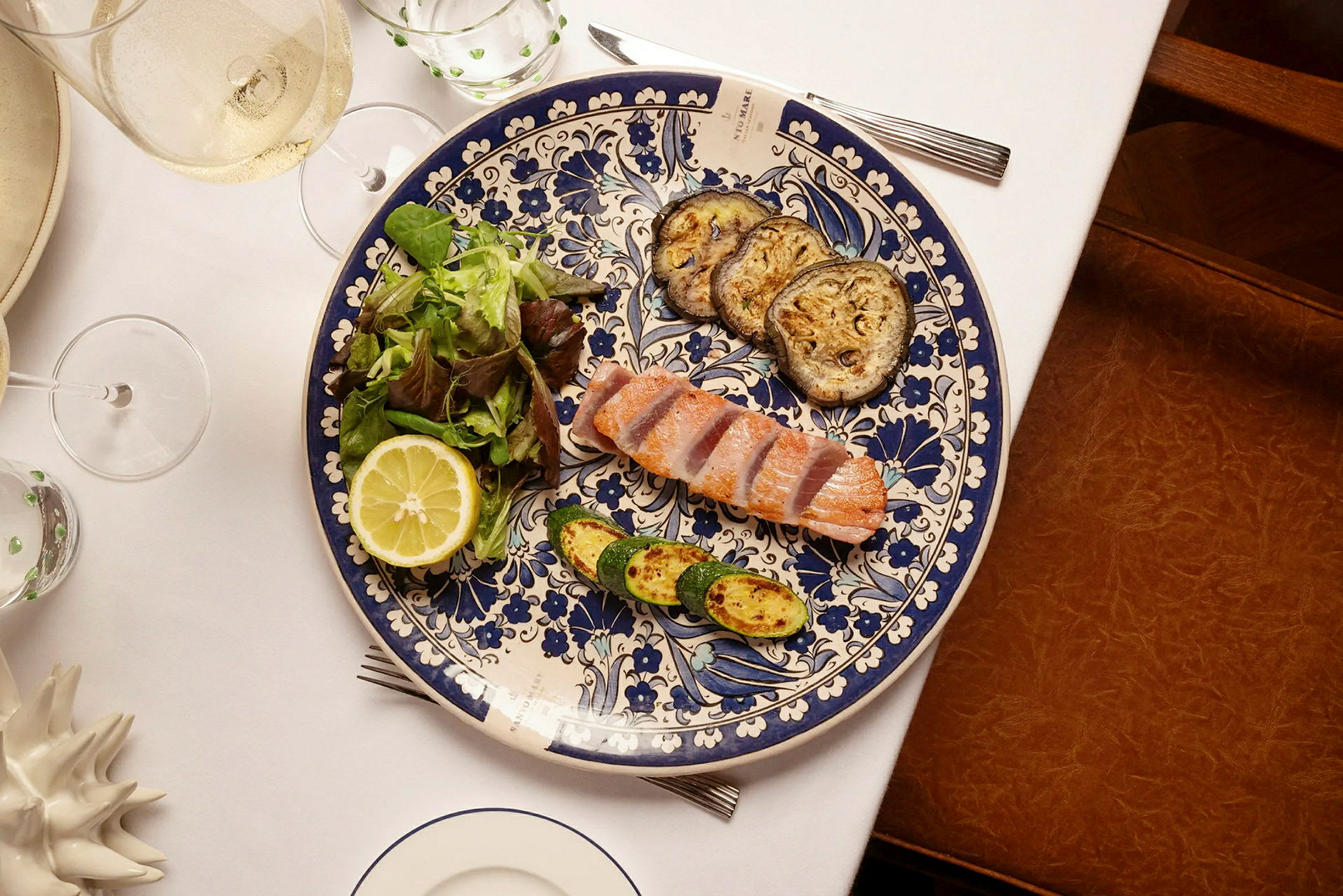 En tallerken med stykker af laks, stegte grøntsager og salat med en halv citron på et dækket bord. (AI-genereret tekst)