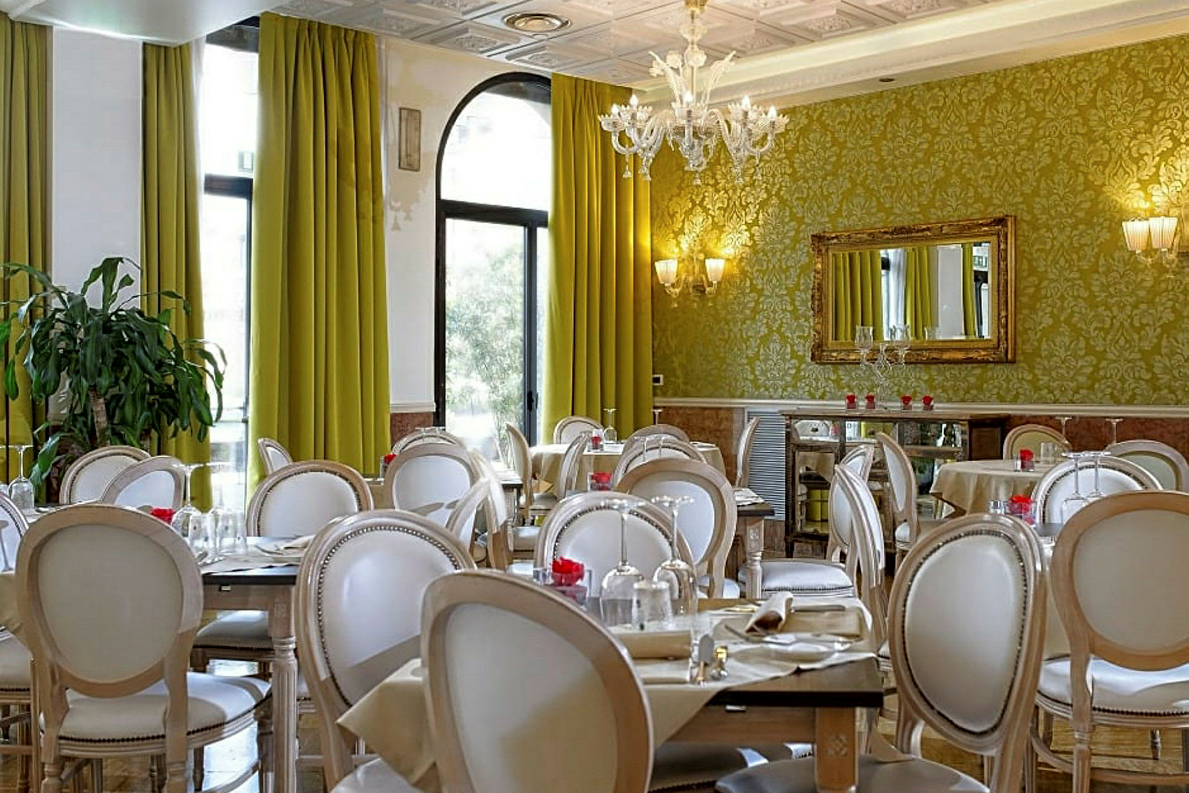 Et elegant indrettet restaurantområde med grønne gardiner, dekorerede vægge og hvide stole omkring dækkede borde. (AI-genereret tekst)