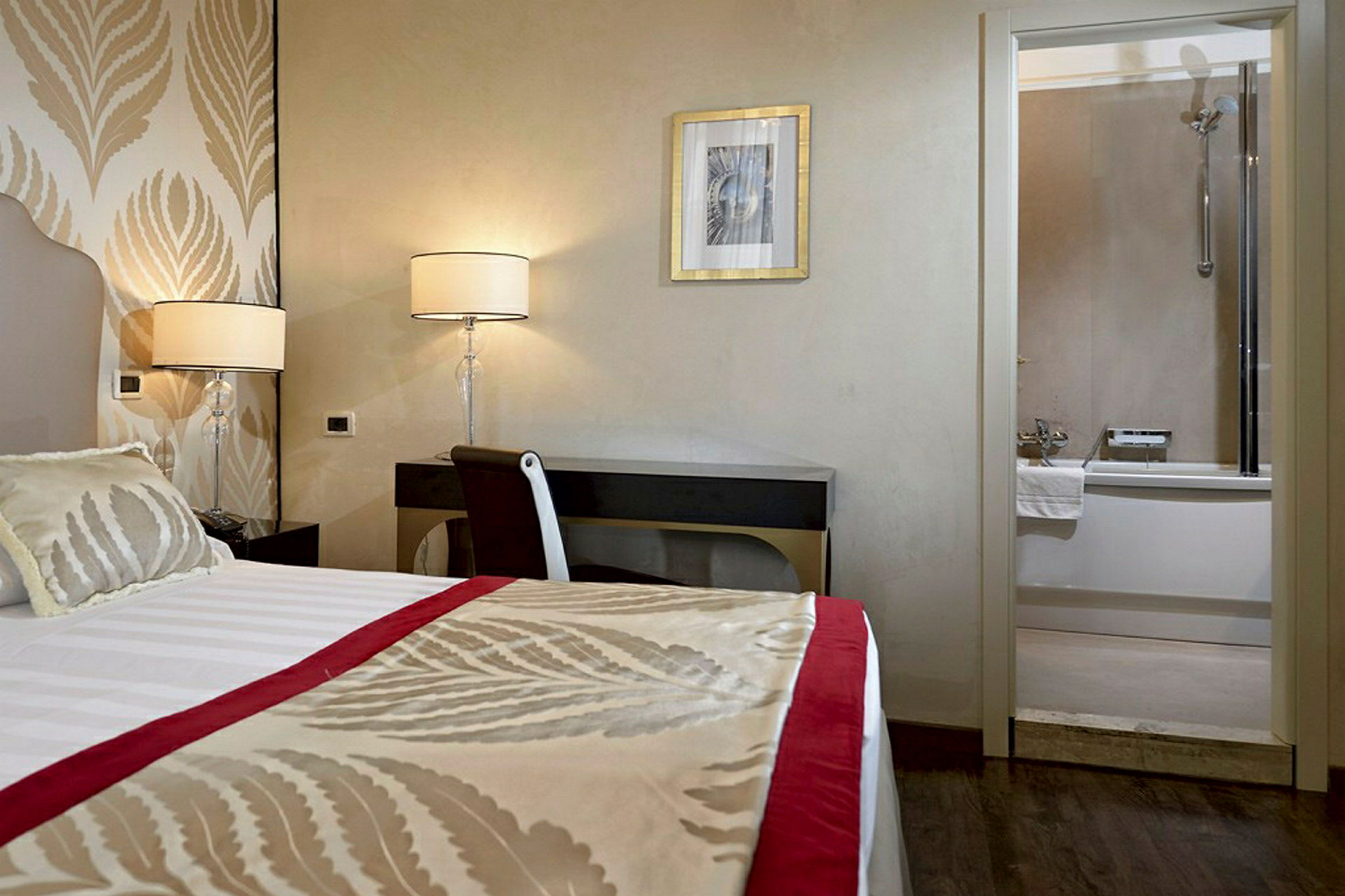 Hotelværelse med en seng, skrivebord og lamper, samt et badeværelse med badekar i baggrunden. (AI-genereret tekst)