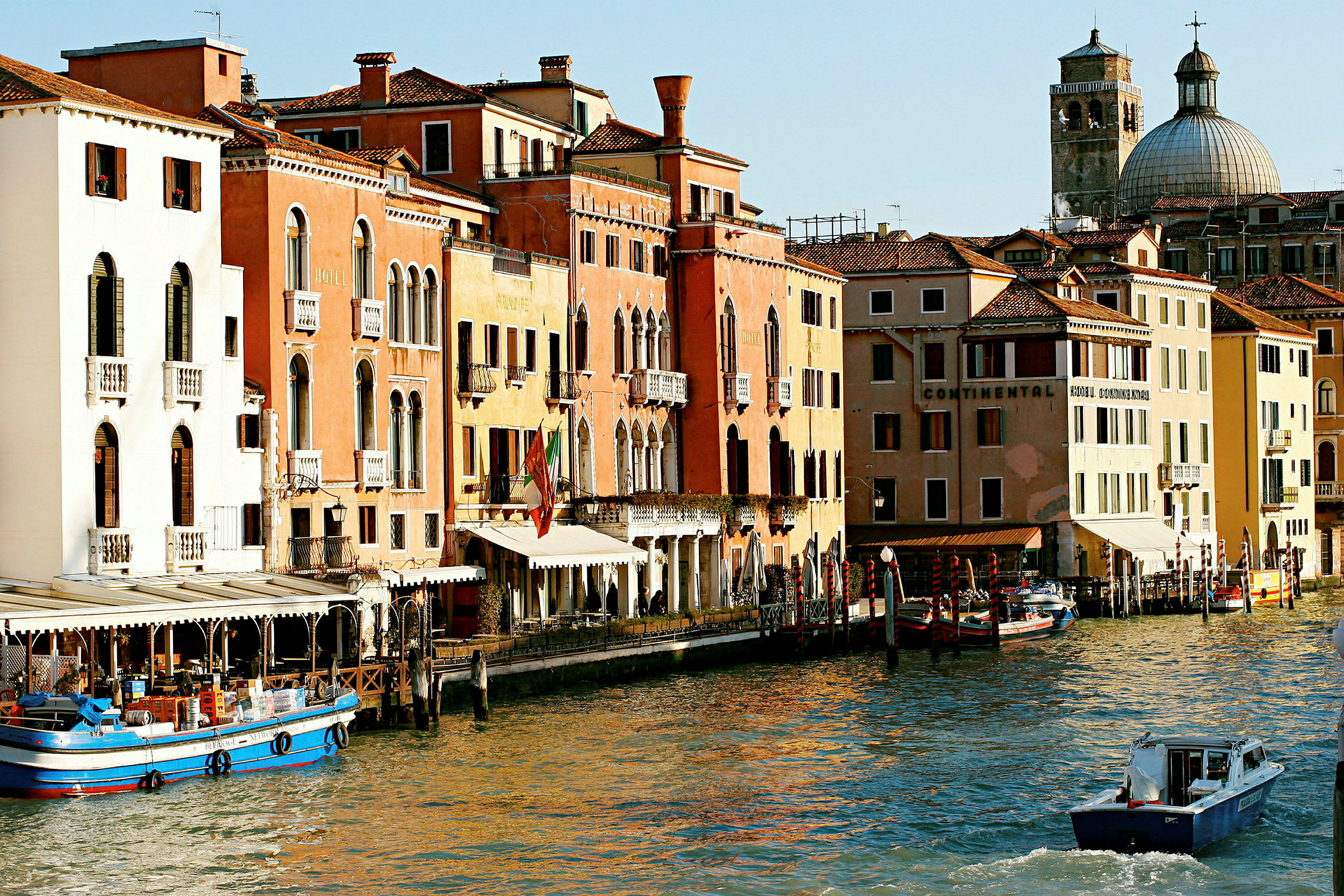 Et billede af en kanal i Venedig med farverige bygninger, både og en kuppelformet kirke i baggrunden. (AI-genereret tekst)