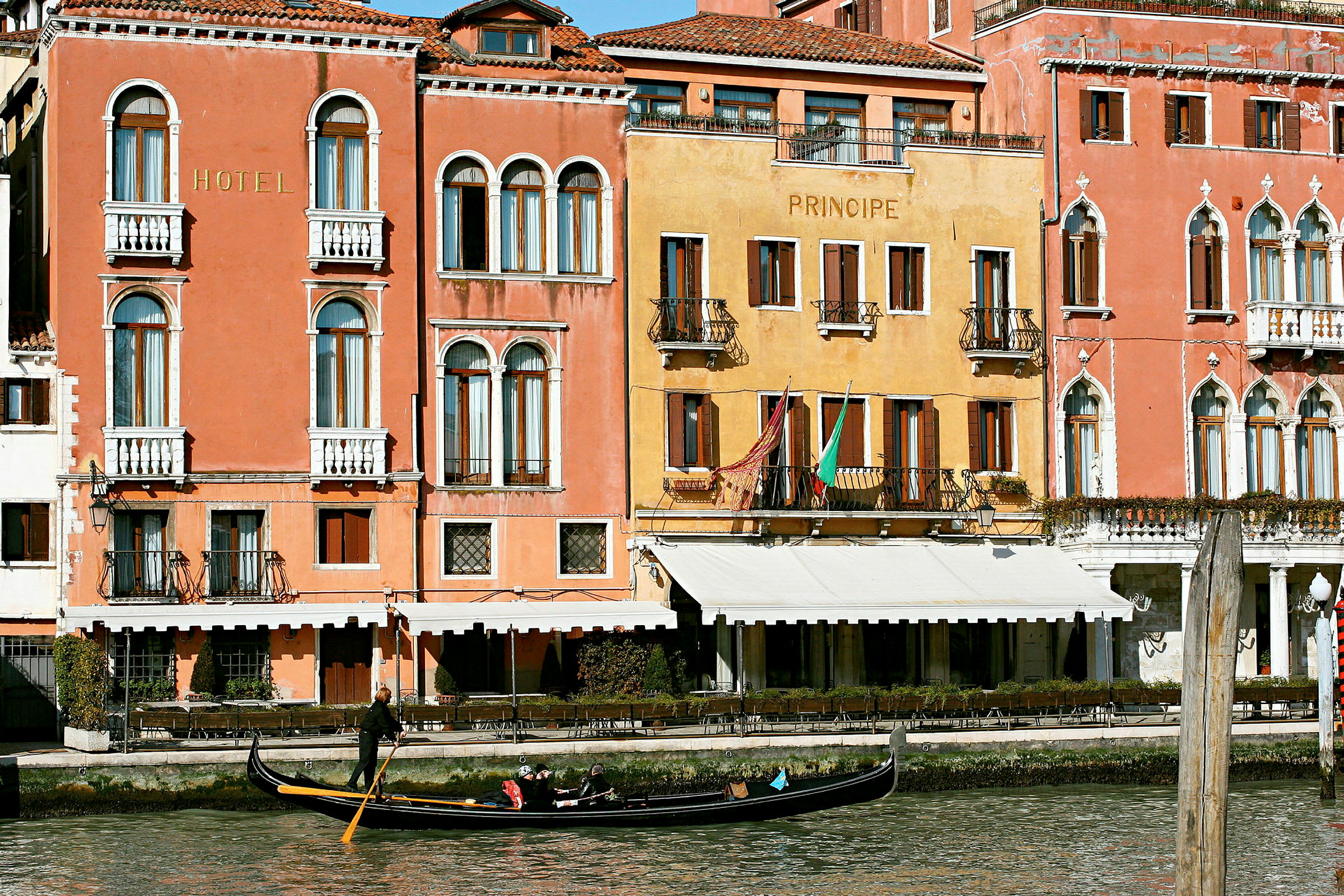 Billede af facaderne på farverige bygninger ved en kanal i Venedig med en gondol på vandet. (AI-genereret tekst)