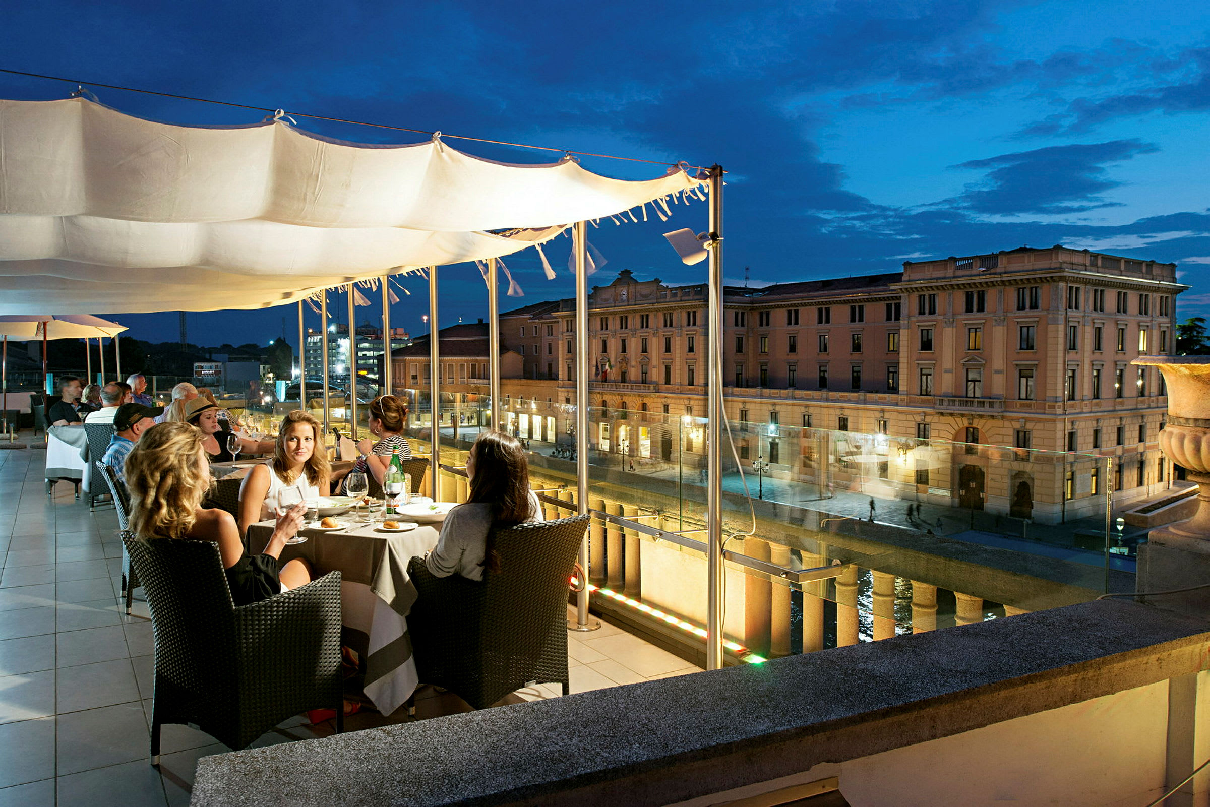 En restaurantterrasse om aftenen med udsigt over en bygade og en klassisk bygning i baggrunden. (AI-genereret tekst)