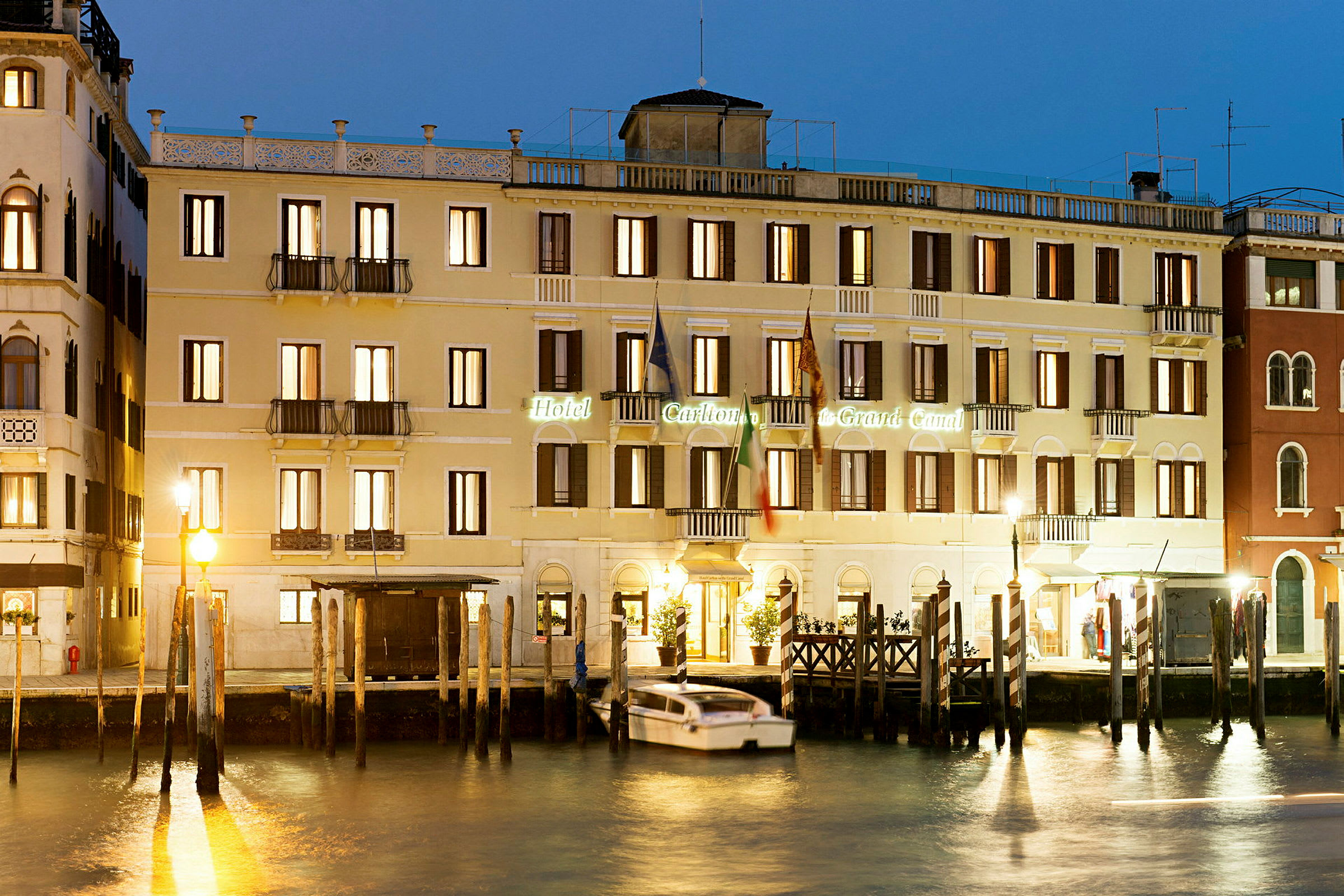 Facade af et oplyst hotel ved en kanal om natten. (AI-genereret tekst)