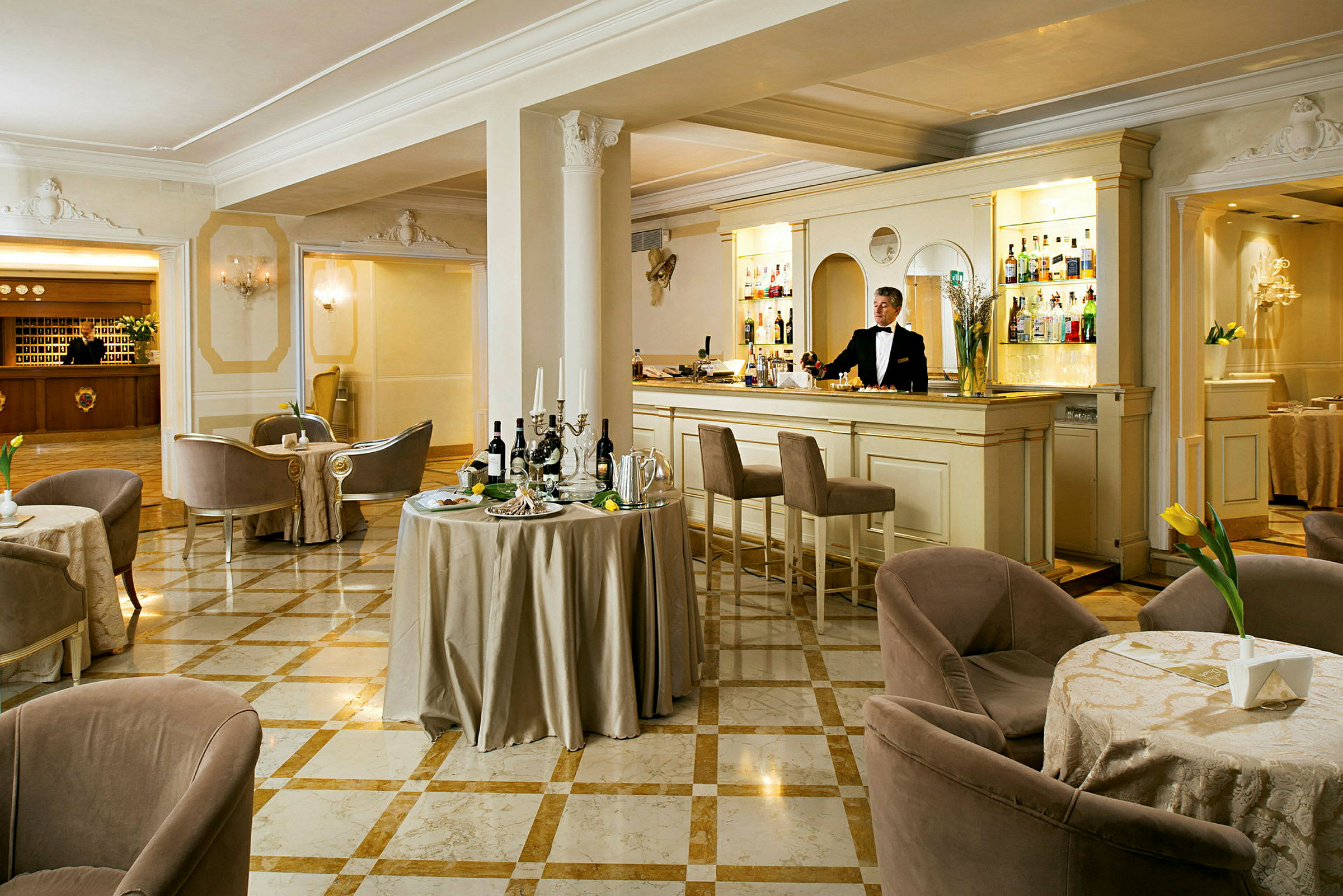 En elegant hotellounge med marmorgulv, små borde og komfortable stole samt en bartender ved skranken. (AI-genereret tekst)