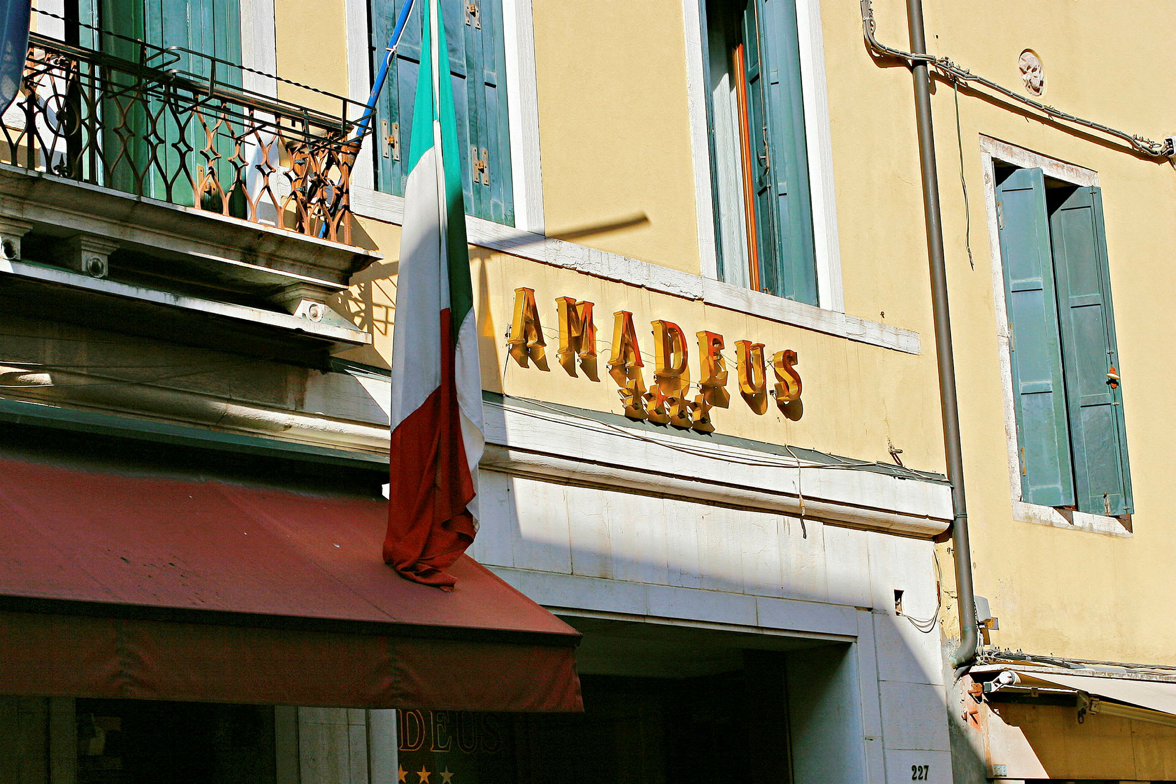 Hotellets facade med et skilt, der siger 'Amadeus', og et italiensk flag. (AI-genereret tekst)