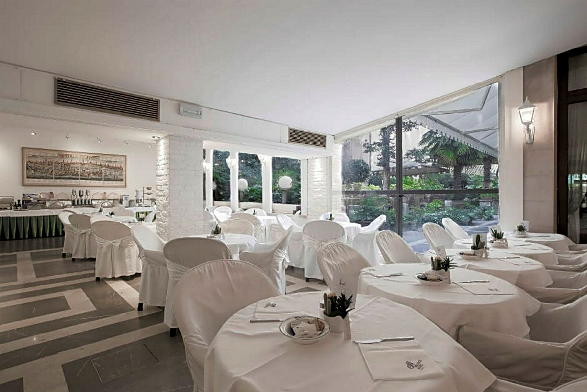 En restaurant med hvide duge og stole, store vinduer og udsigt til en frodig have. (AI-genereret tekst)