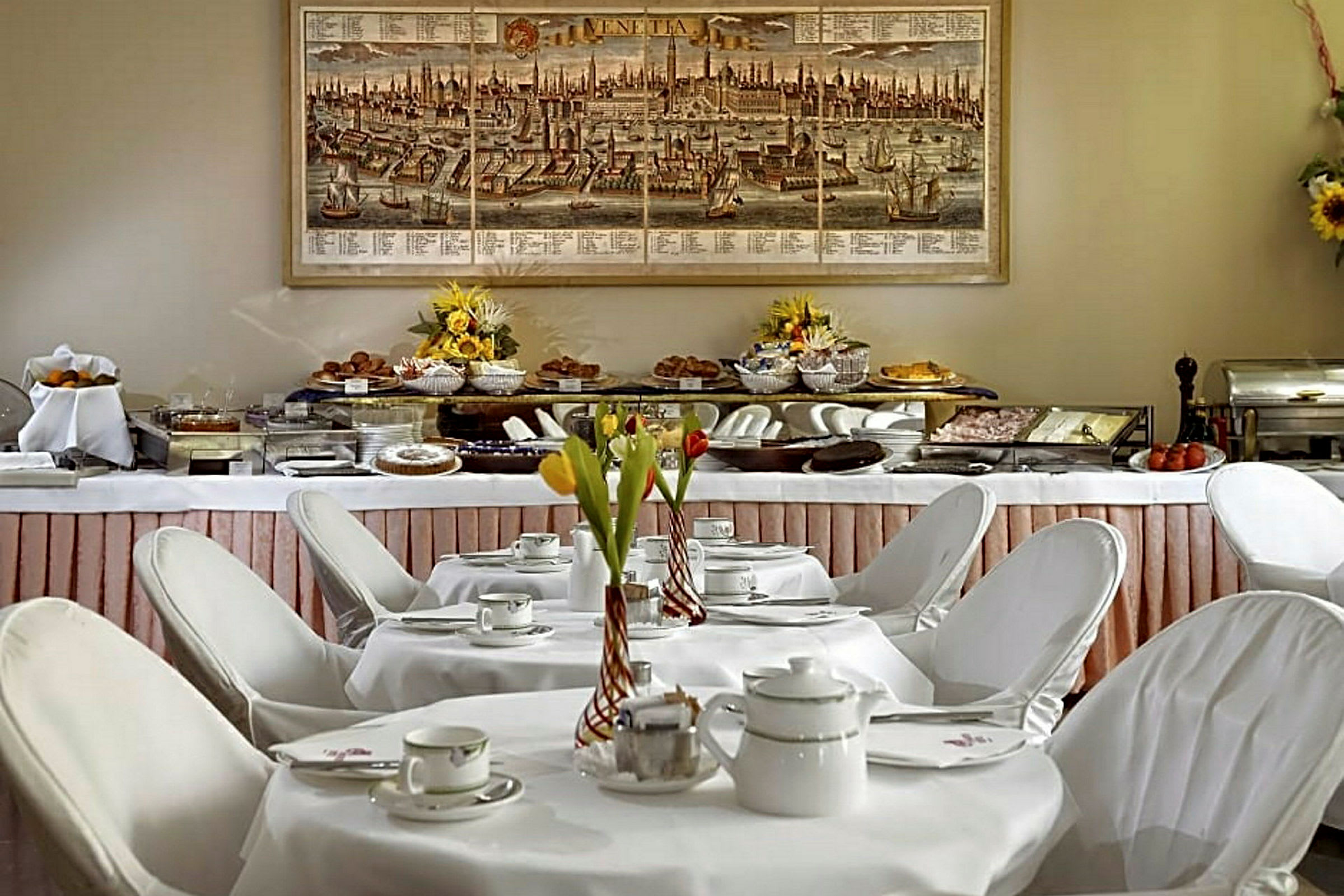 Et morgenmadsbord dækket med porcelæn og blomsterdekorationer foran en buffet fyldt med retter. (AI-genereret tekst)