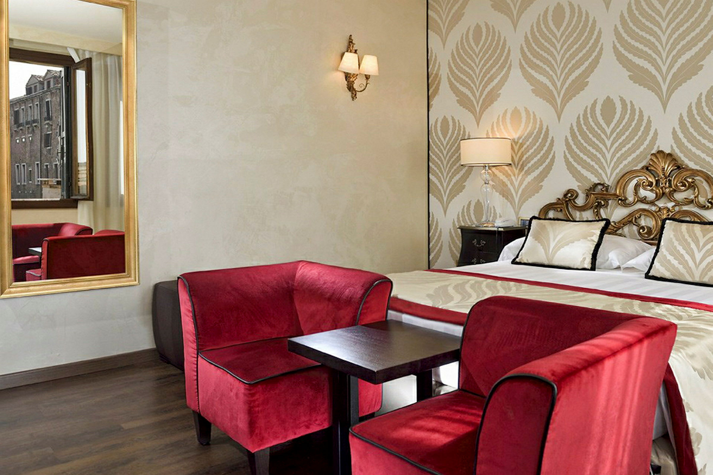 Et elegant hotelværelse med en dobbeltseng, røde lænestole og et lille bord samt et vindue med udsigt. (AI-genereret tekst)