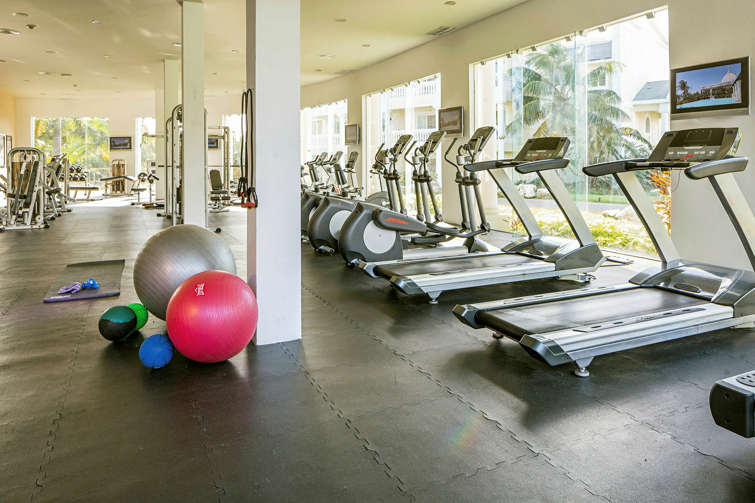 Fitnesssal med træningsmaskiner, løbebånd og træningsbolde. (AI-genereret tekst)