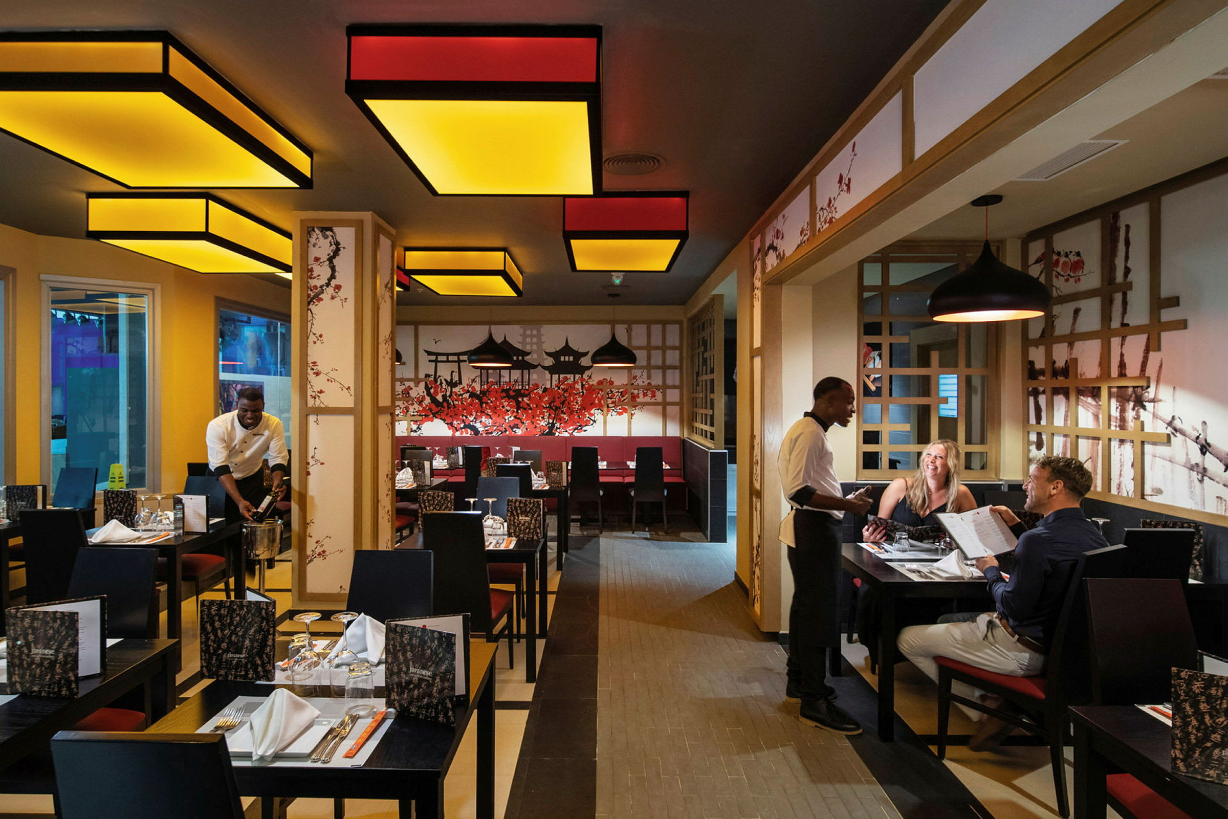 En restaurant med udsmykning inspireret af asiatisk kultur og personale, der betjener gæster. (AI-genereret tekst)