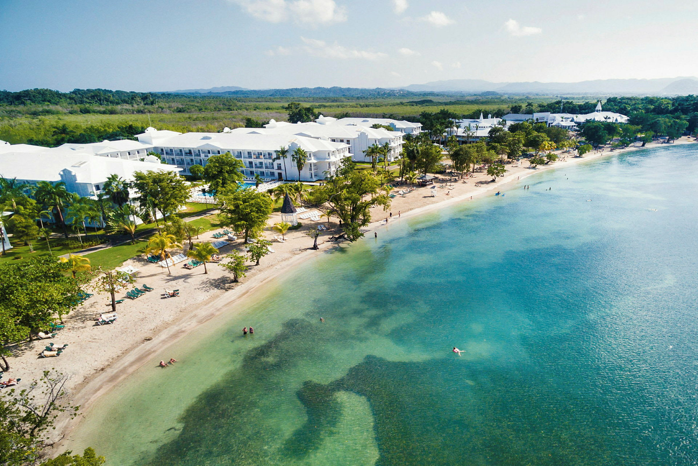Billede af en strand med klart blåt vand og hotelbygninger i baggrunden. (AI-genereret tekst)