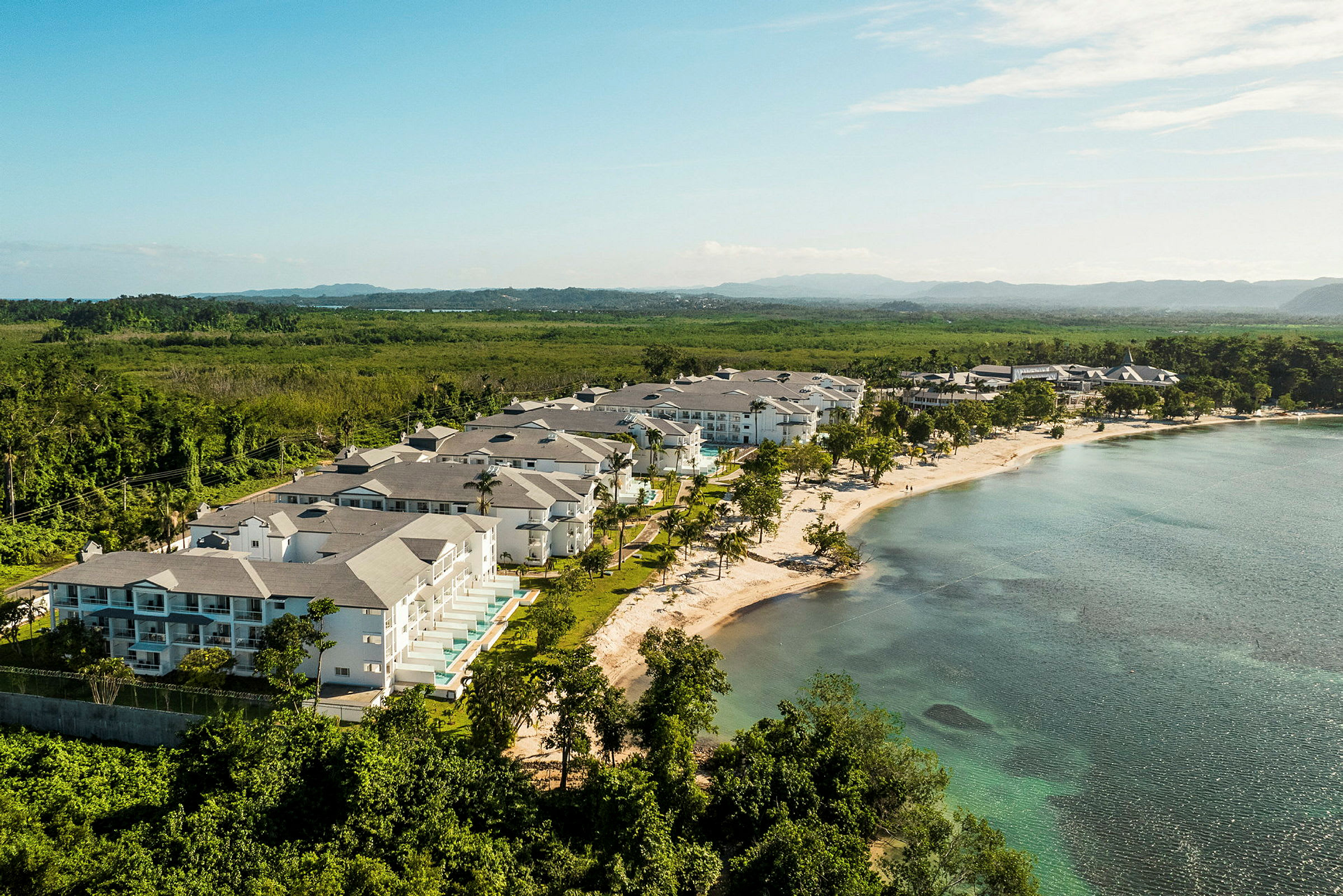 Et strandområde med resortbygninger omgivet af grønne områder og hav. (AI-genereret tekst)