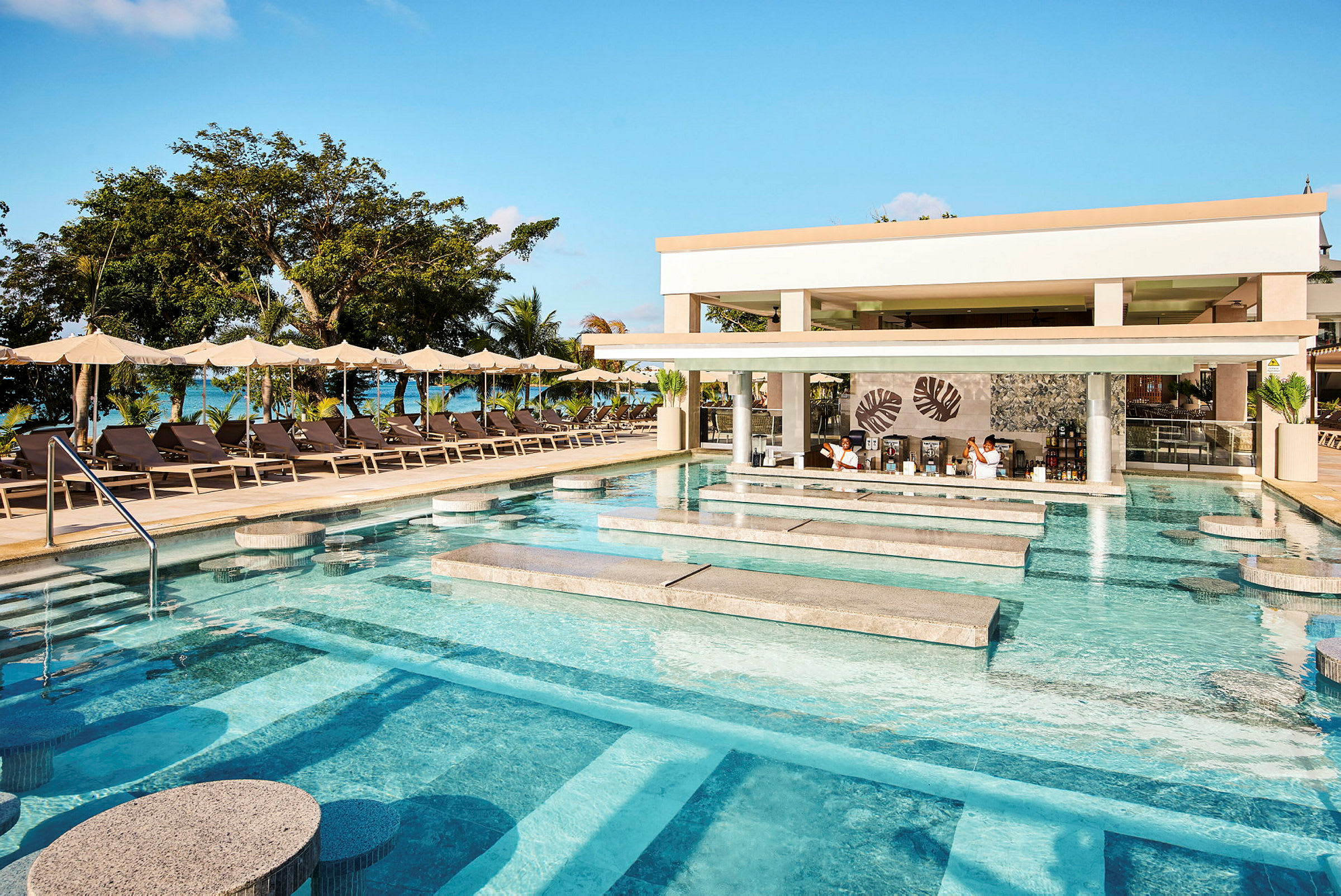 En pool med siddepladser og en swim-up bar ved en resort med liggestole og parasoller i baggrunden. (AI-genereret tekst)