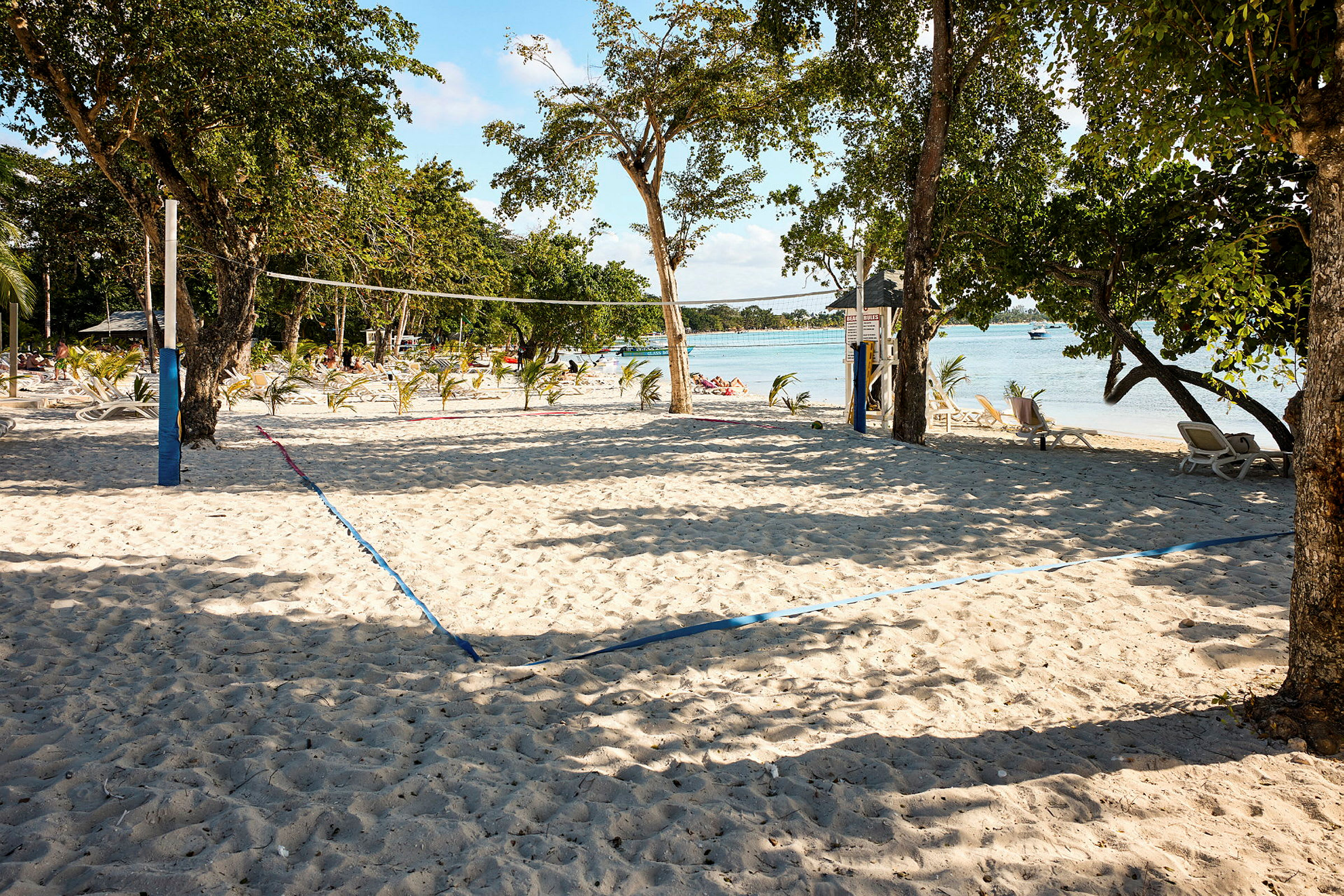 En sandstrand med volleyballnet og stole i baggrunden. (AI-genereret tekst)