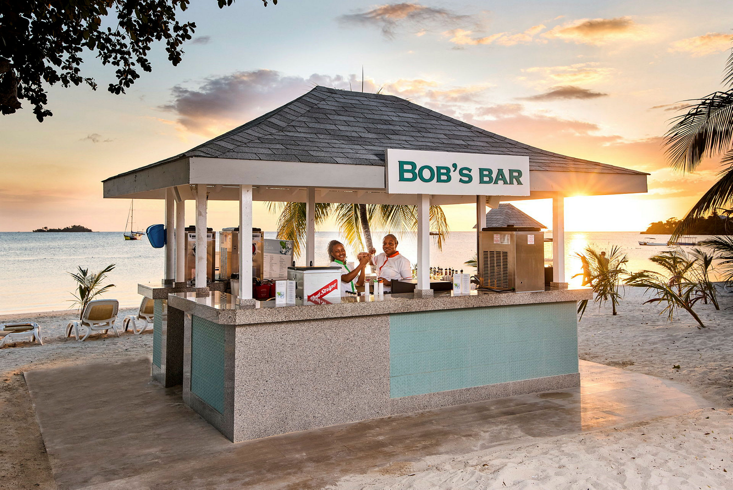 Strandbar med tag og skilt med teksten 'Bob's Bar', omgivet af palmer og med havudsigt. (AI-genereret tekst)