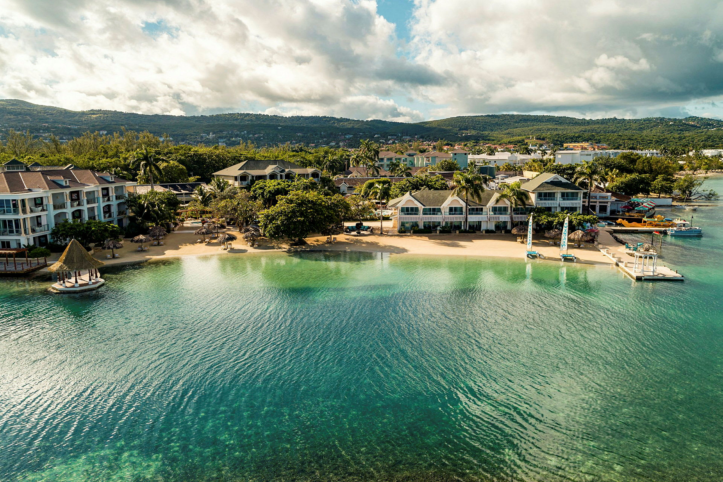 Luftfoto af en strand med hotelbygninger og grønne områder. (AI-genereret tekst)