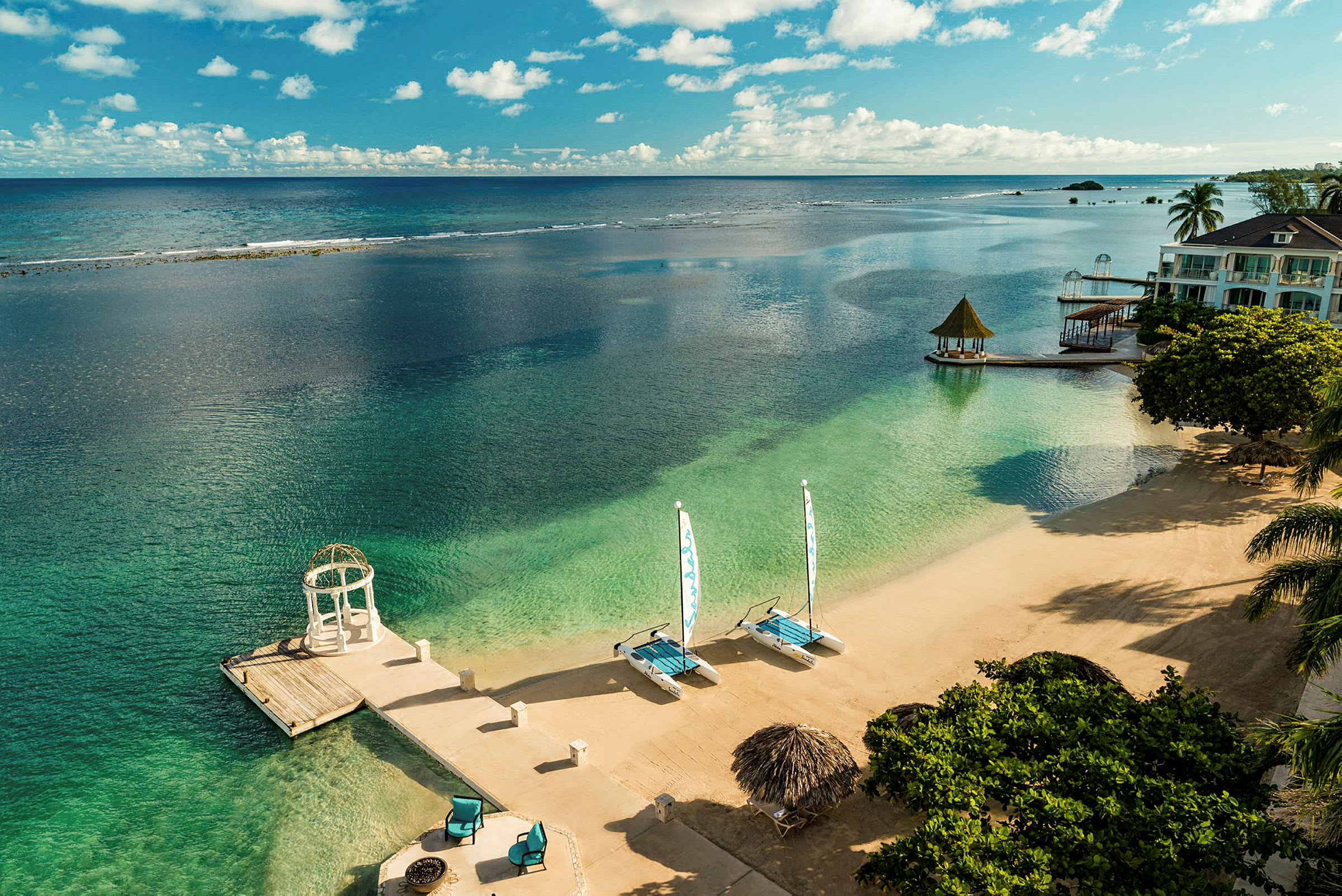 Strand med klart vand, liggestole og sejlbåde. (AI-genereret tekst)