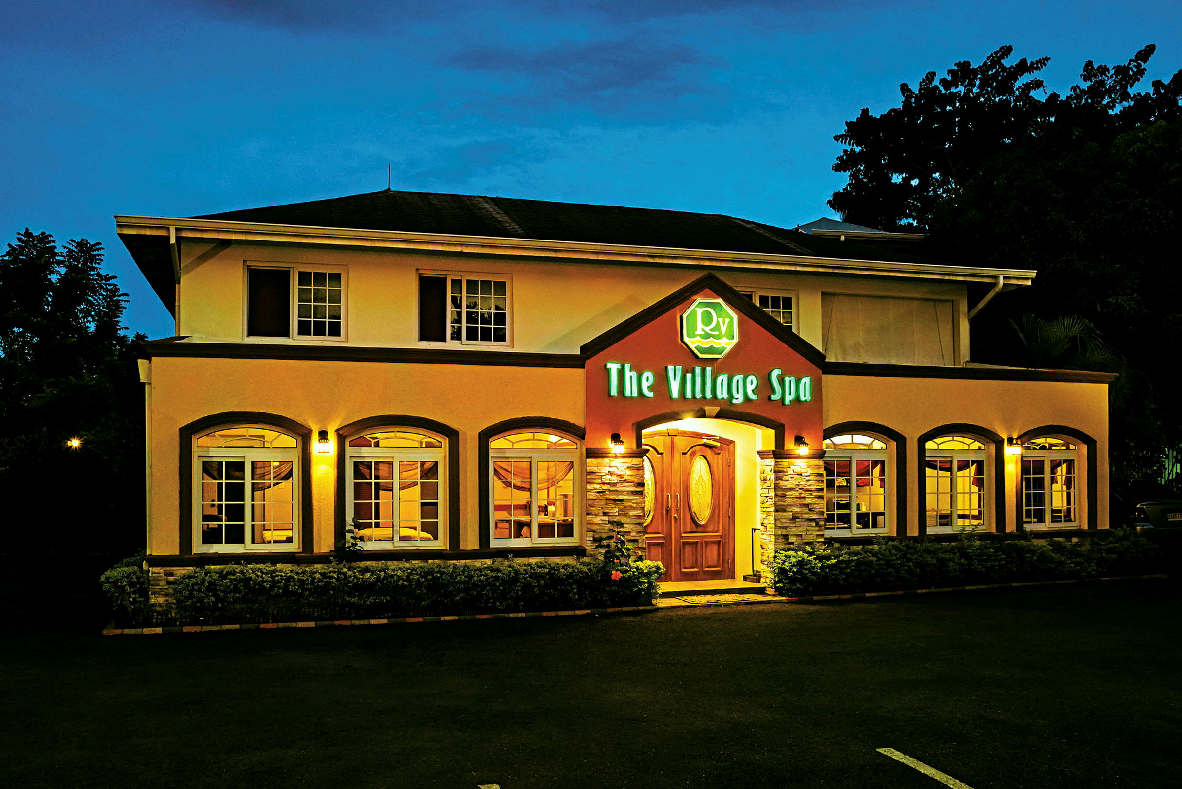 Bygning med to etager, oplyst facade og indgang med et skilt, der viser navnet "The Village Spa". (AI-genereret tekst)