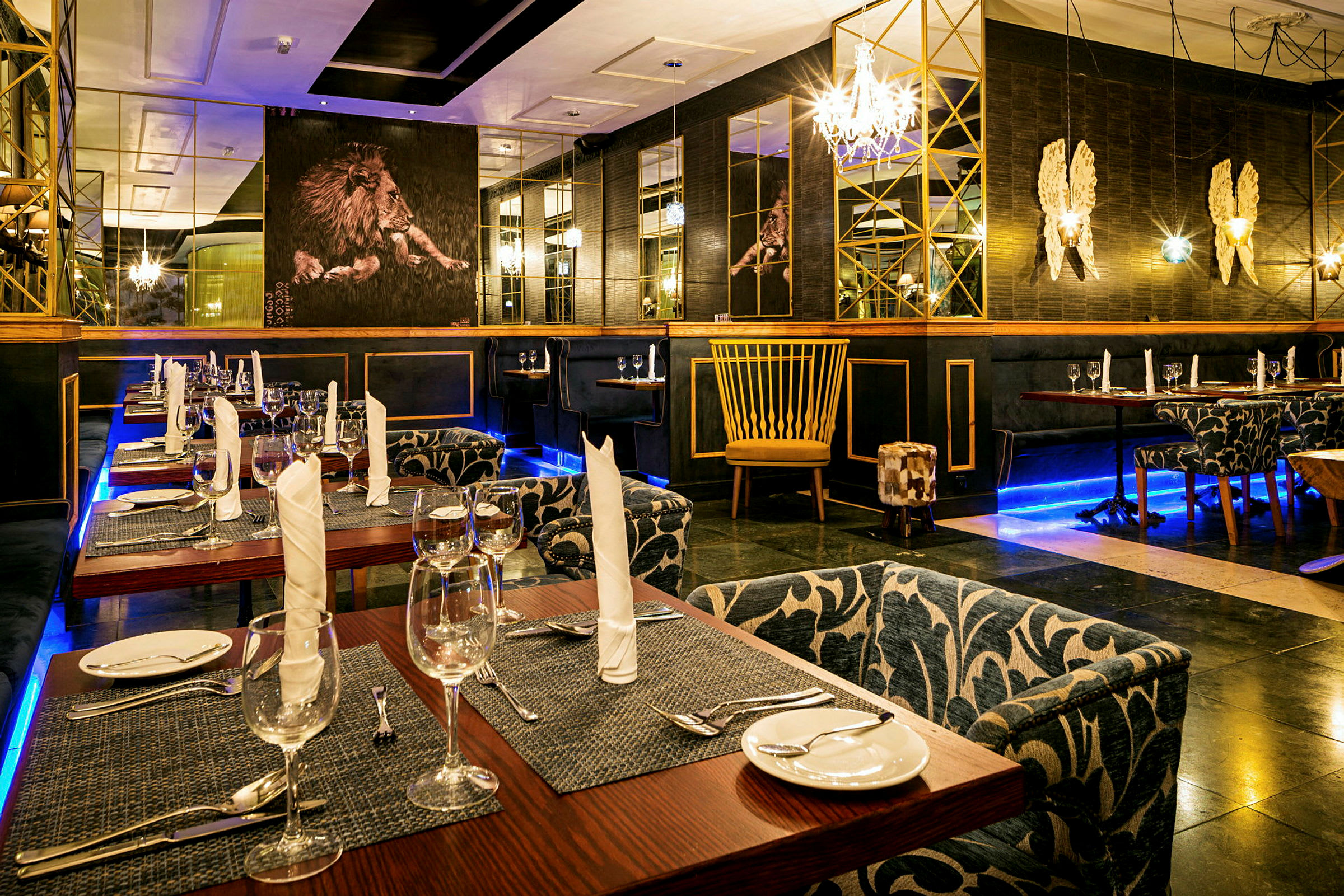 Interiørbillede af en restaurant med dækkede borde, elegante stole og dekorative detaljer såsom spejle og løvemotiv på en væg. (AI-genereret tekst)