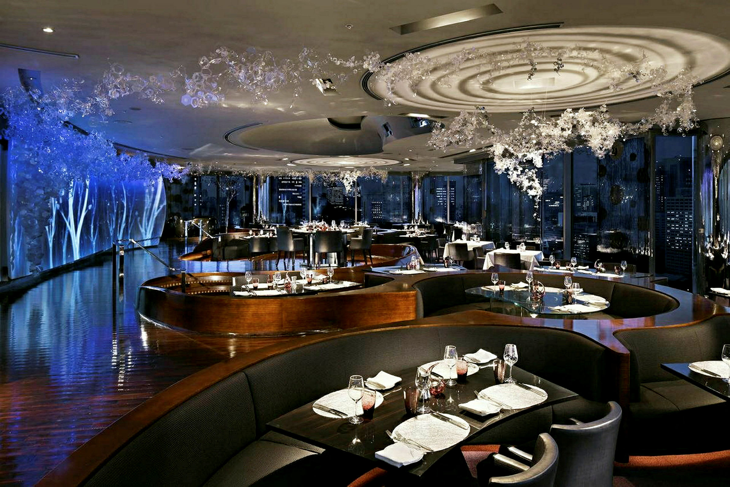 En elegant restaurant med stilfuld indretning, hvor bordene er pænt dækket og omgivet af mørke siddepladser. (AI-genereret tekst)