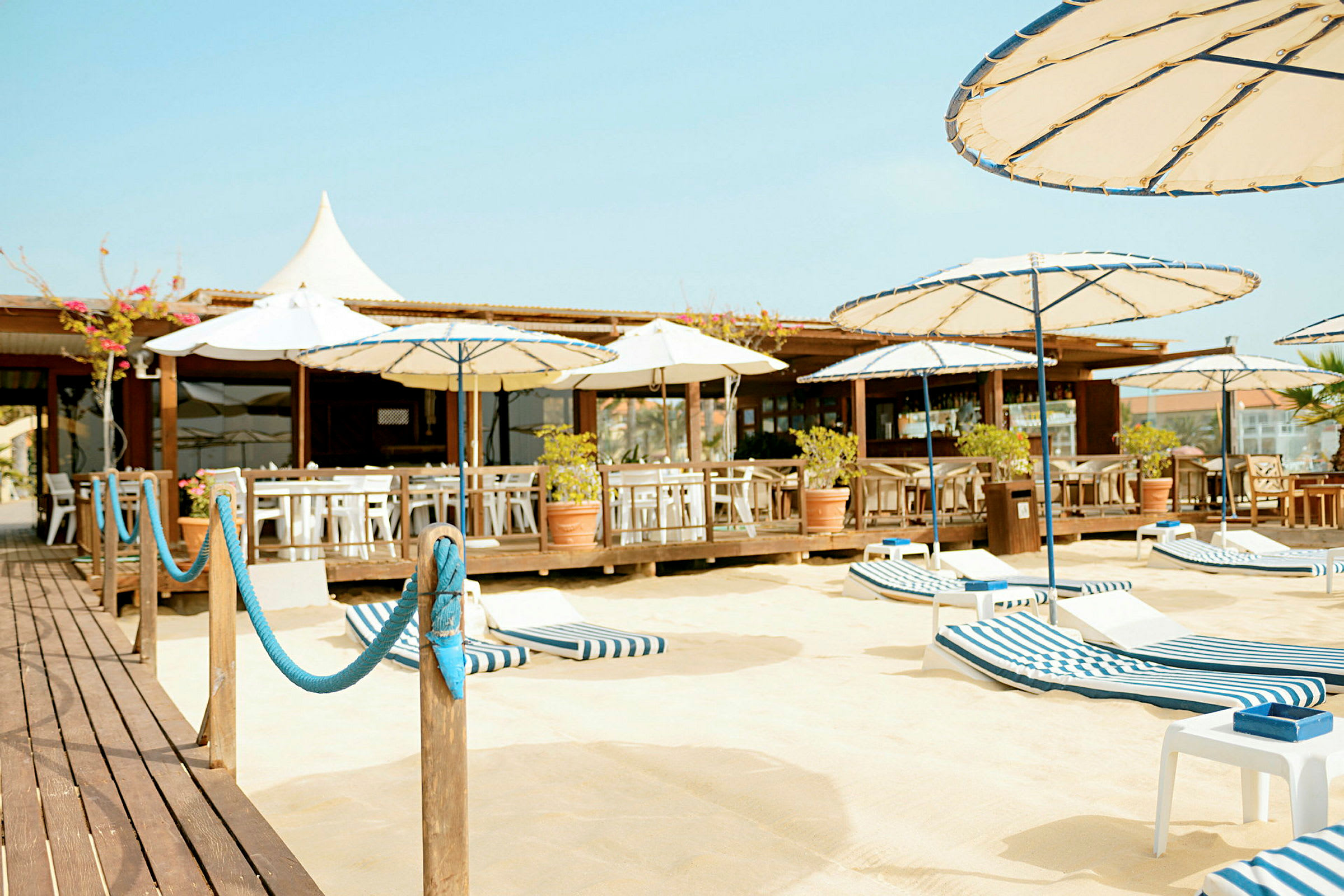 En strandbar med siddepladser, parasoller og liggestole på en sandet overflade. (AI-genereret tekst)
