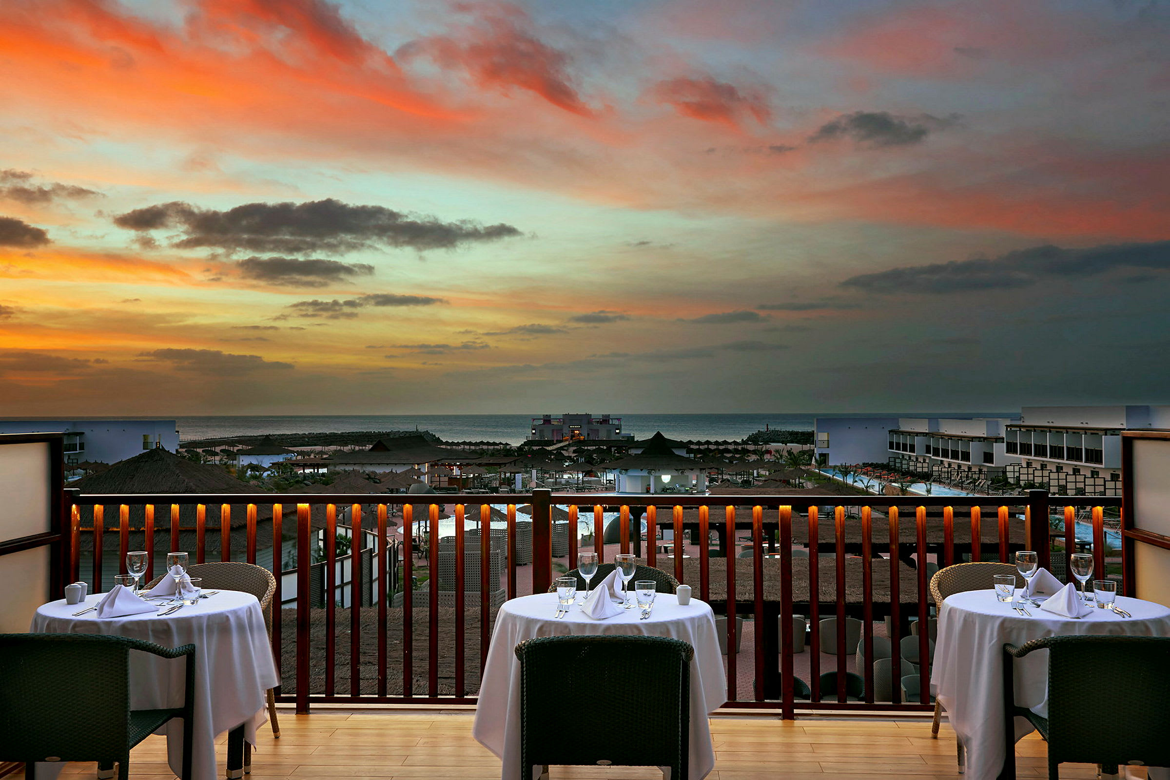Udsigt fra en restaurant med dækkede borde mod solnedgangen over havet. (AI-genereret tekst)