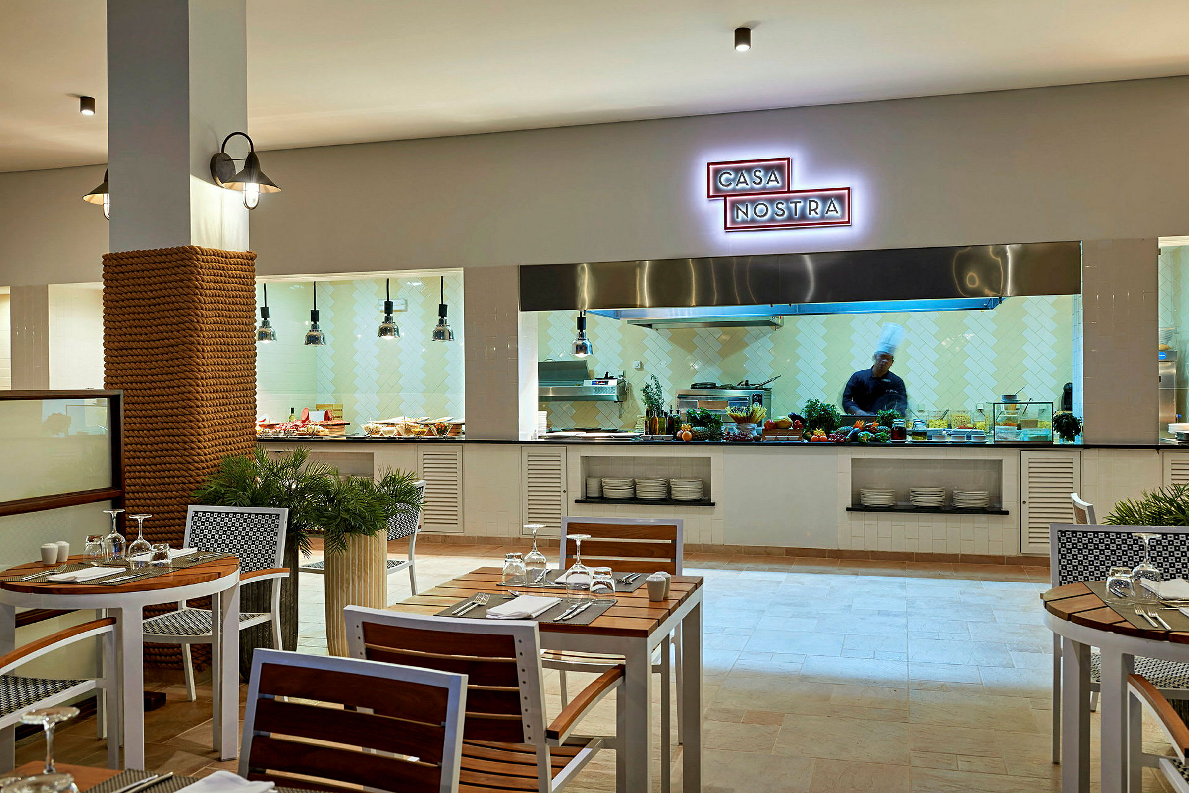 Restaurant med køkkenområde i baggrunden og opdækkede borde i forgrunden. (AI-genereret tekst)