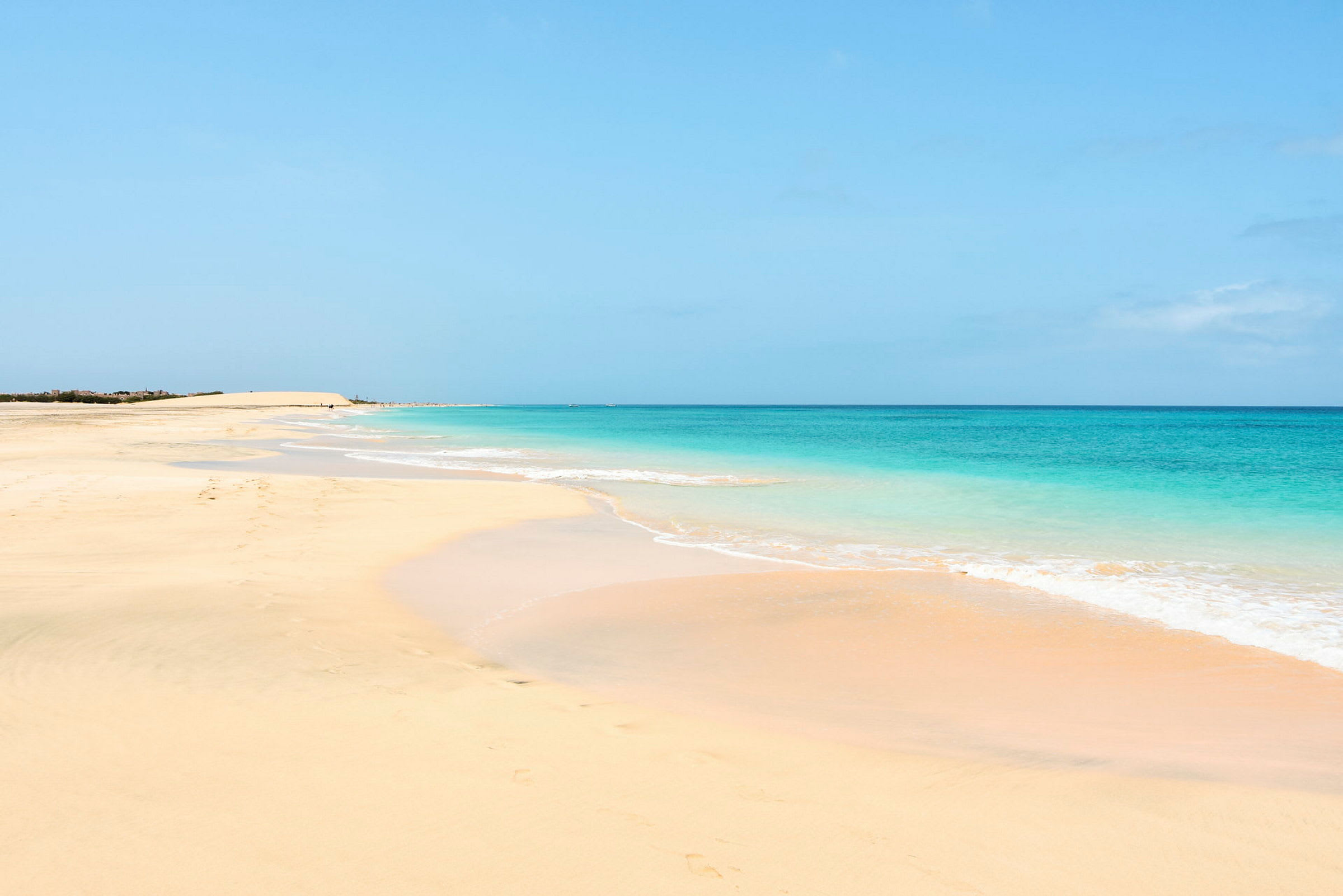 En sandstrand med blåt hav og klar himmel. (AI-genereret tekst)