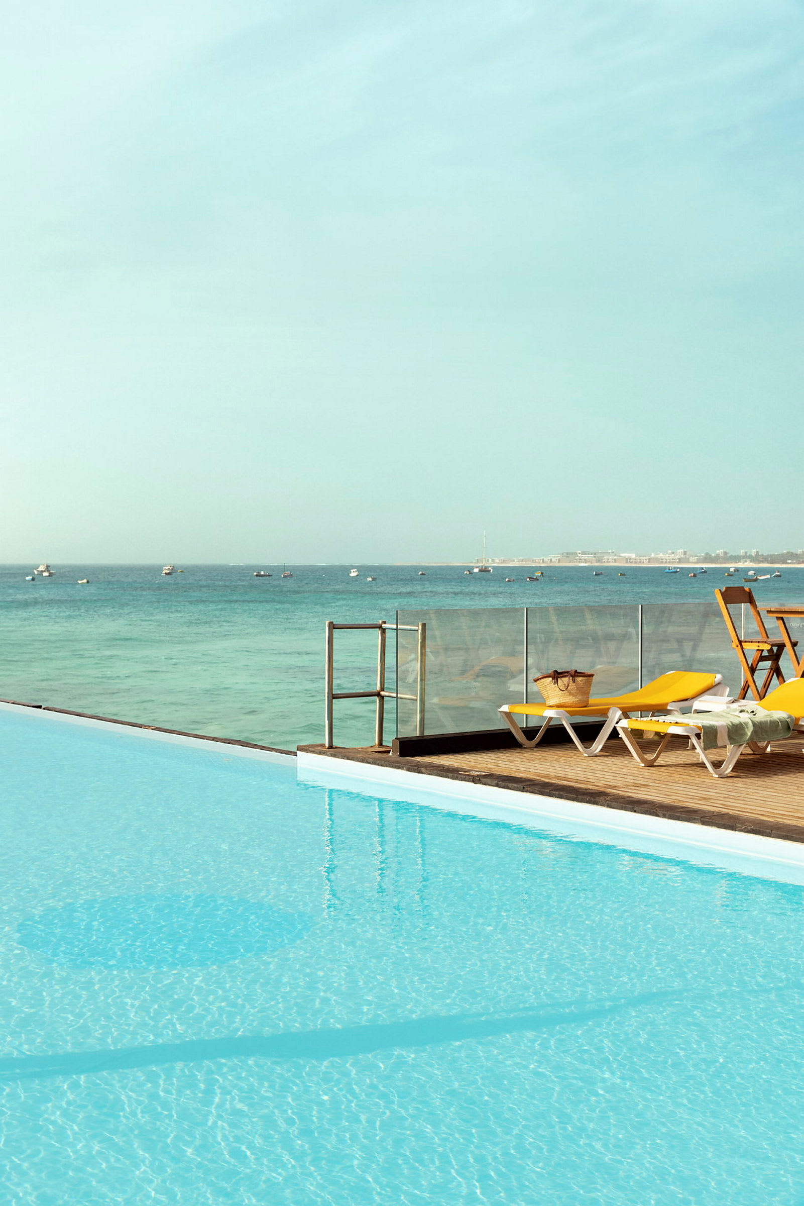 Swimmingpool med udsigt over havet. Liggestole og bord med stole på terrassen. (AI-genereret tekst)