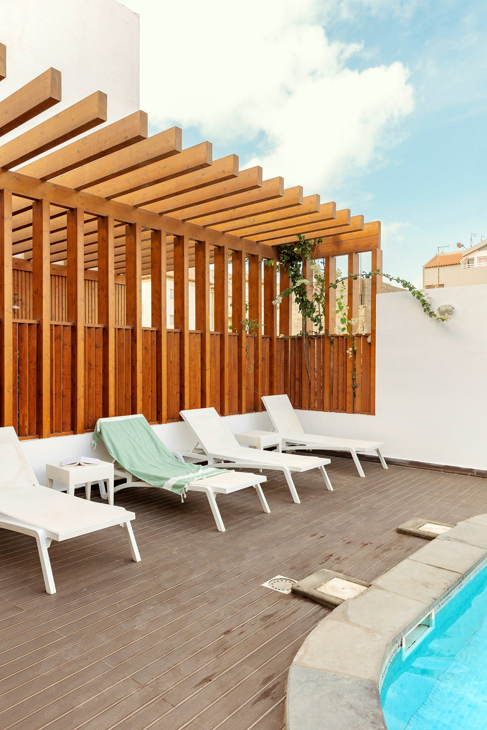 Liggestole på en terrasse ved en pool med trægulv og pergola. (AI-genereret tekst)