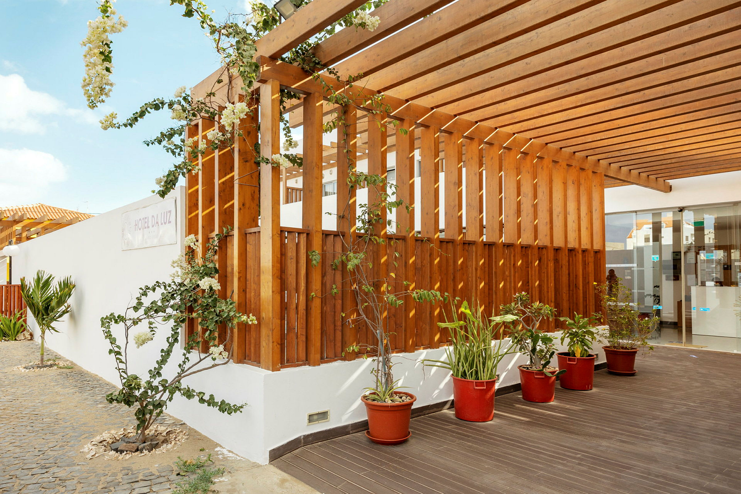 Træpergola med klatreplanter og potteplanter ved en bygning. (AI-genereret tekst)