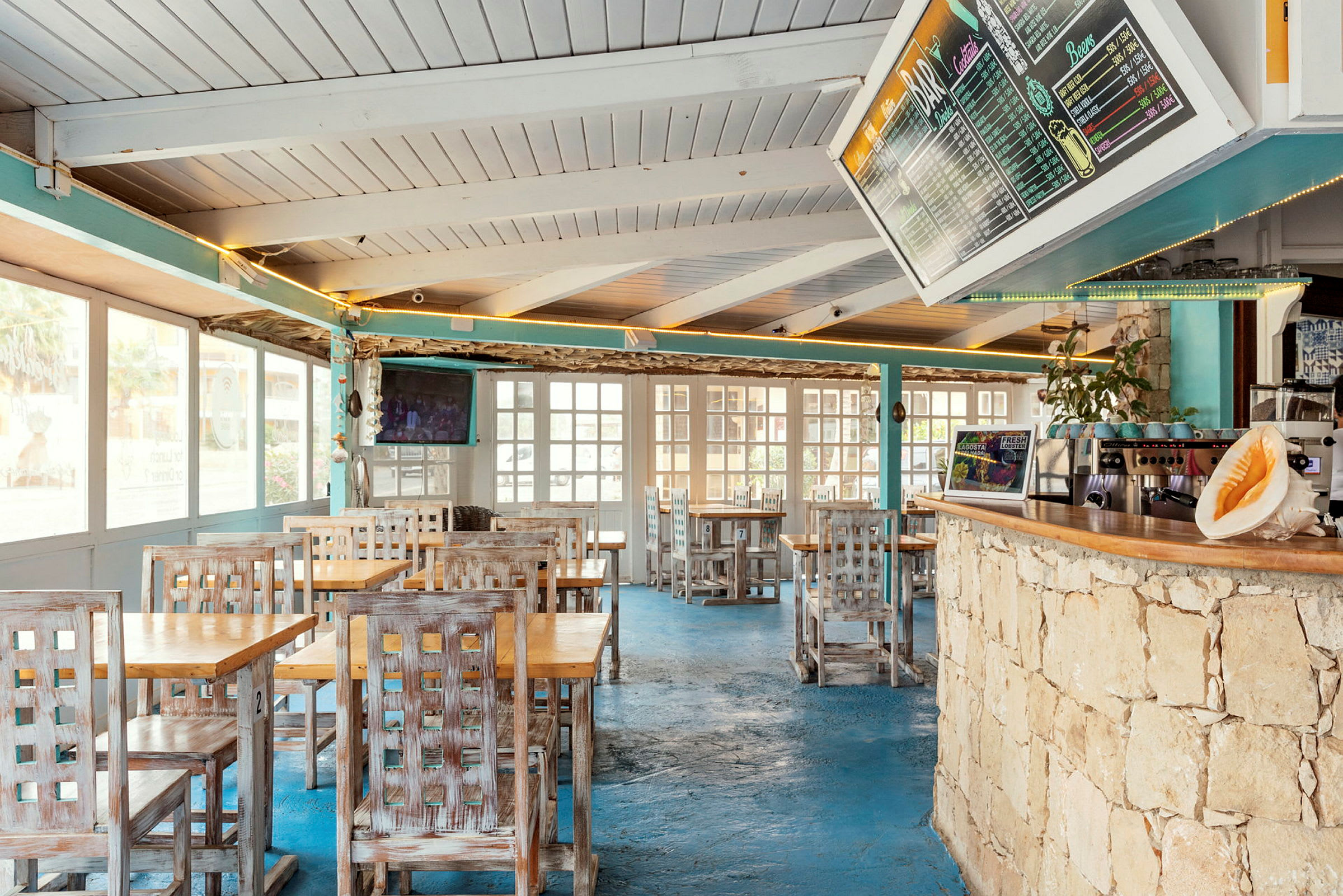 Interiør af en restaurant med træborde og stole, blå gulv og en menu på væggen. (AI-genereret tekst)