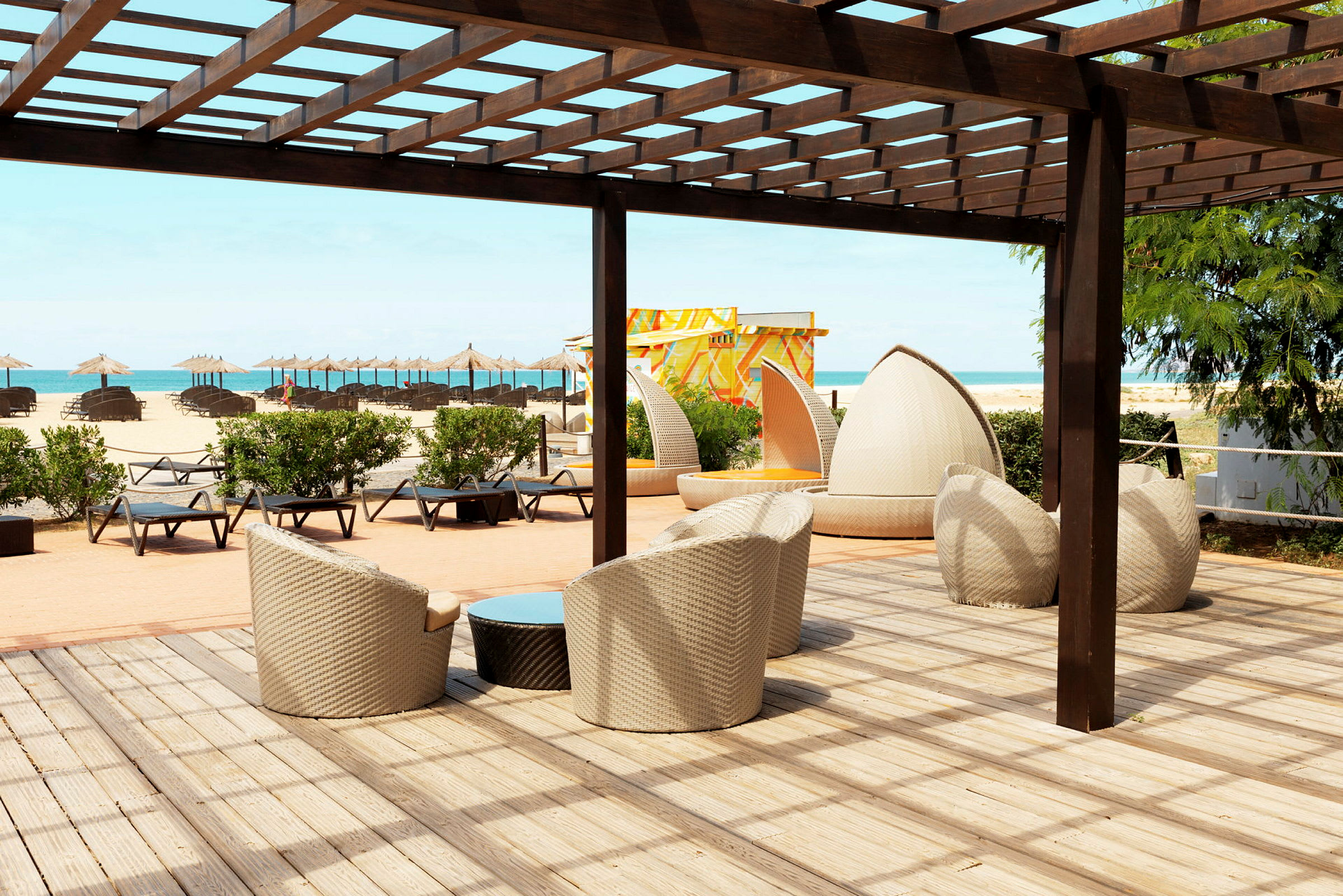 Loungeområde med siddepladser under en pergola tæt på stranden. (AI-genereret tekst)
