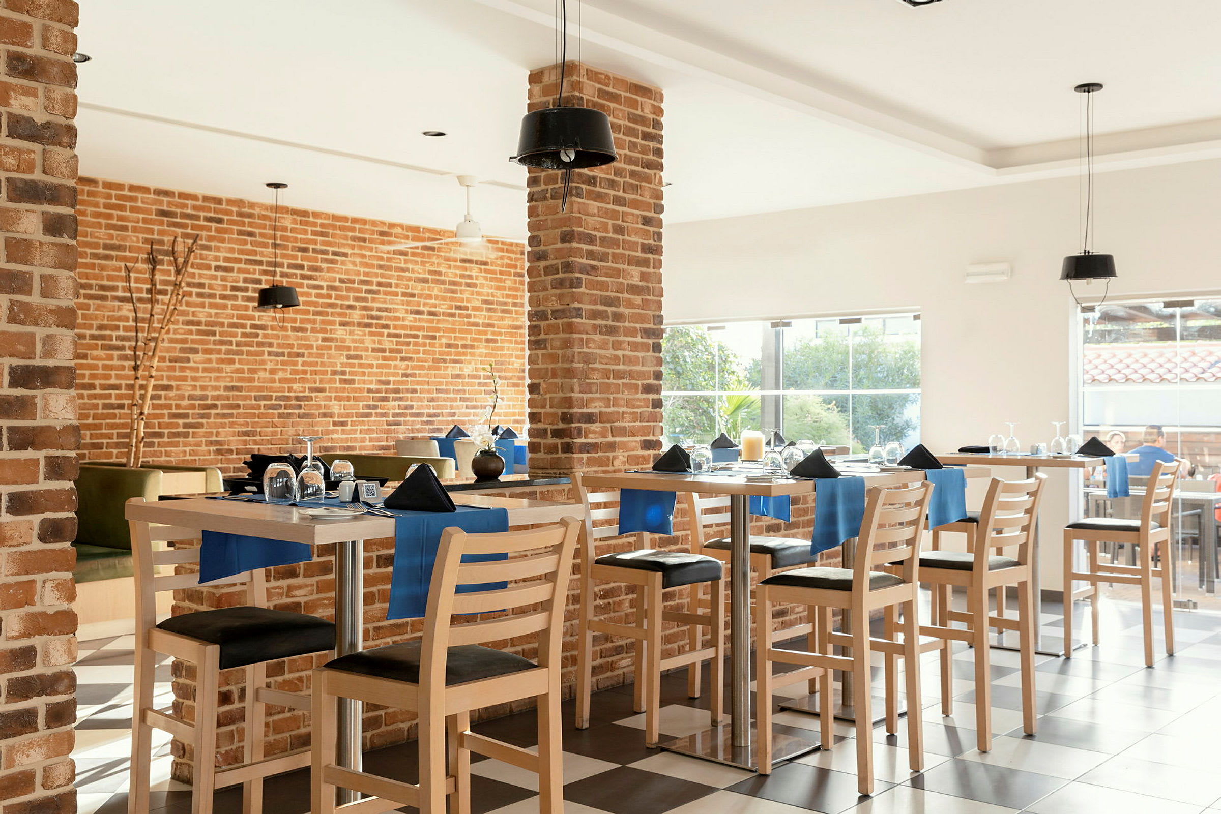 Interiør af en restaurant med murstensvægge, fuldt møbleret med borde og stole dekoreret med blå detaljer. (AI-genereret tekst)