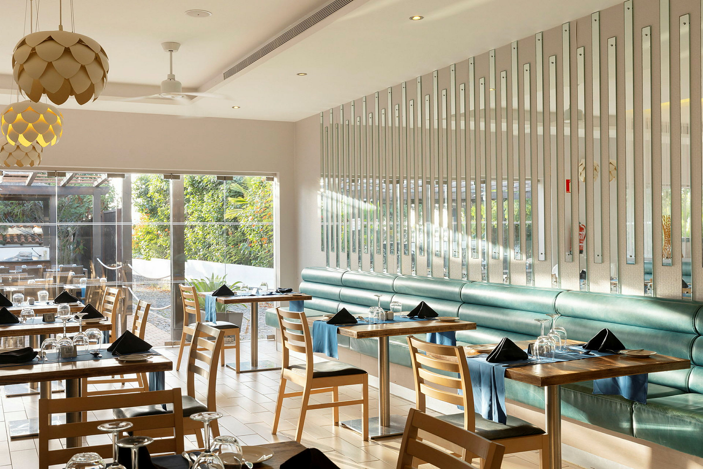 En moderne og lys restaurantindretning med borde og stole, hvor vinduer vender mod et frodigt udendørsområde. (AI-genereret tekst)