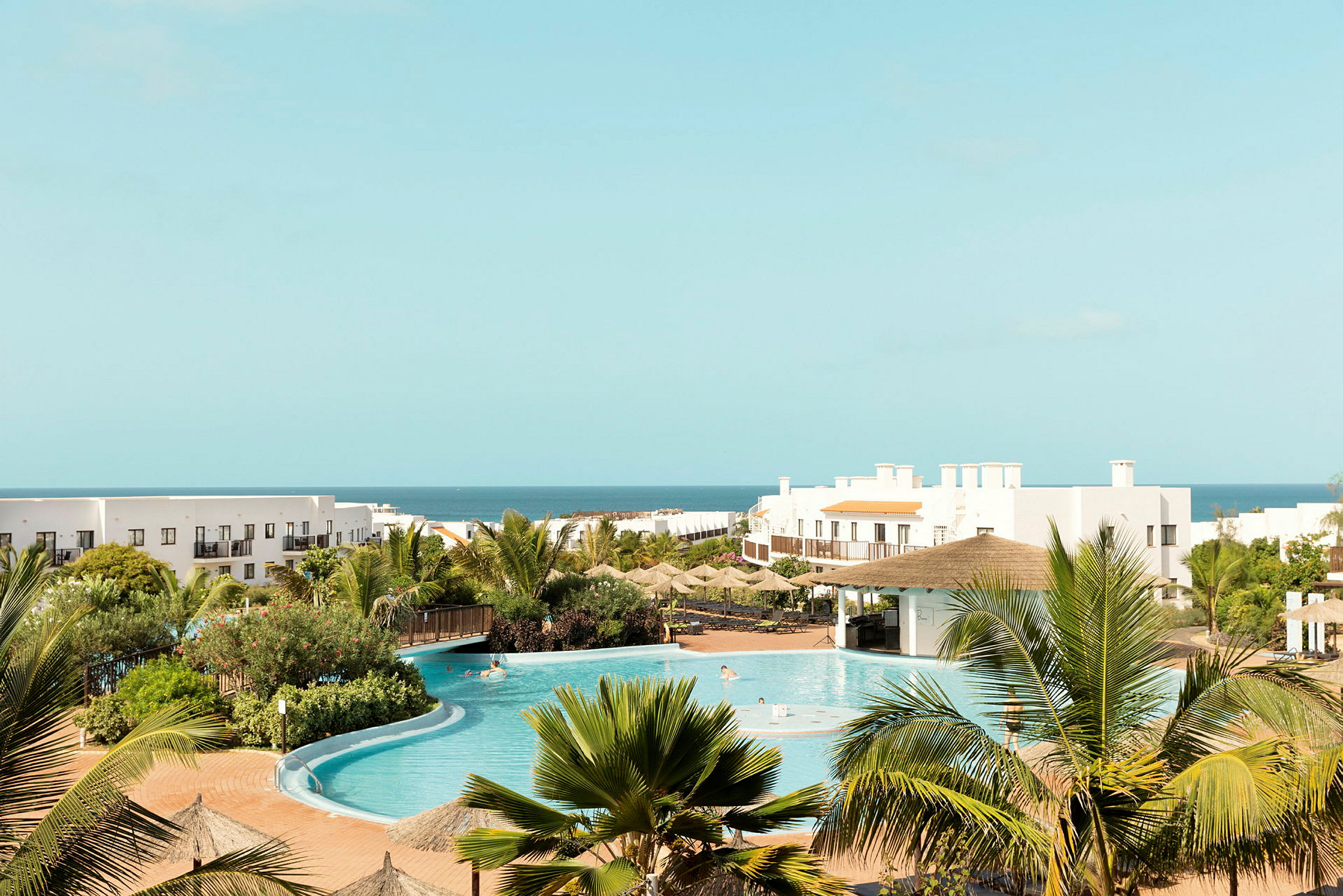 Hotelområde med pool, grønne omgivelser og havet i baggrunden. (AI-genereret tekst)